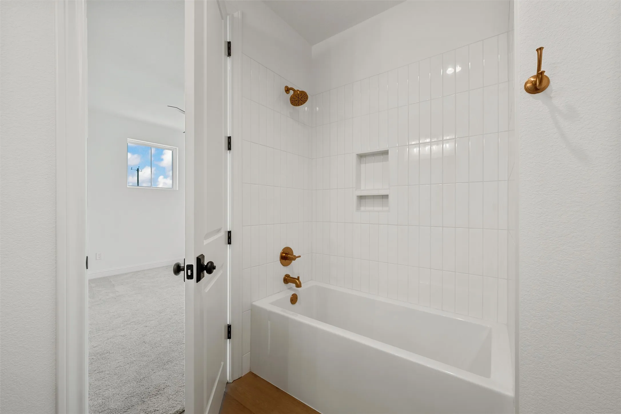 Bathtub with vertical white subway tile surround, recessed shelving, and brass fixtures