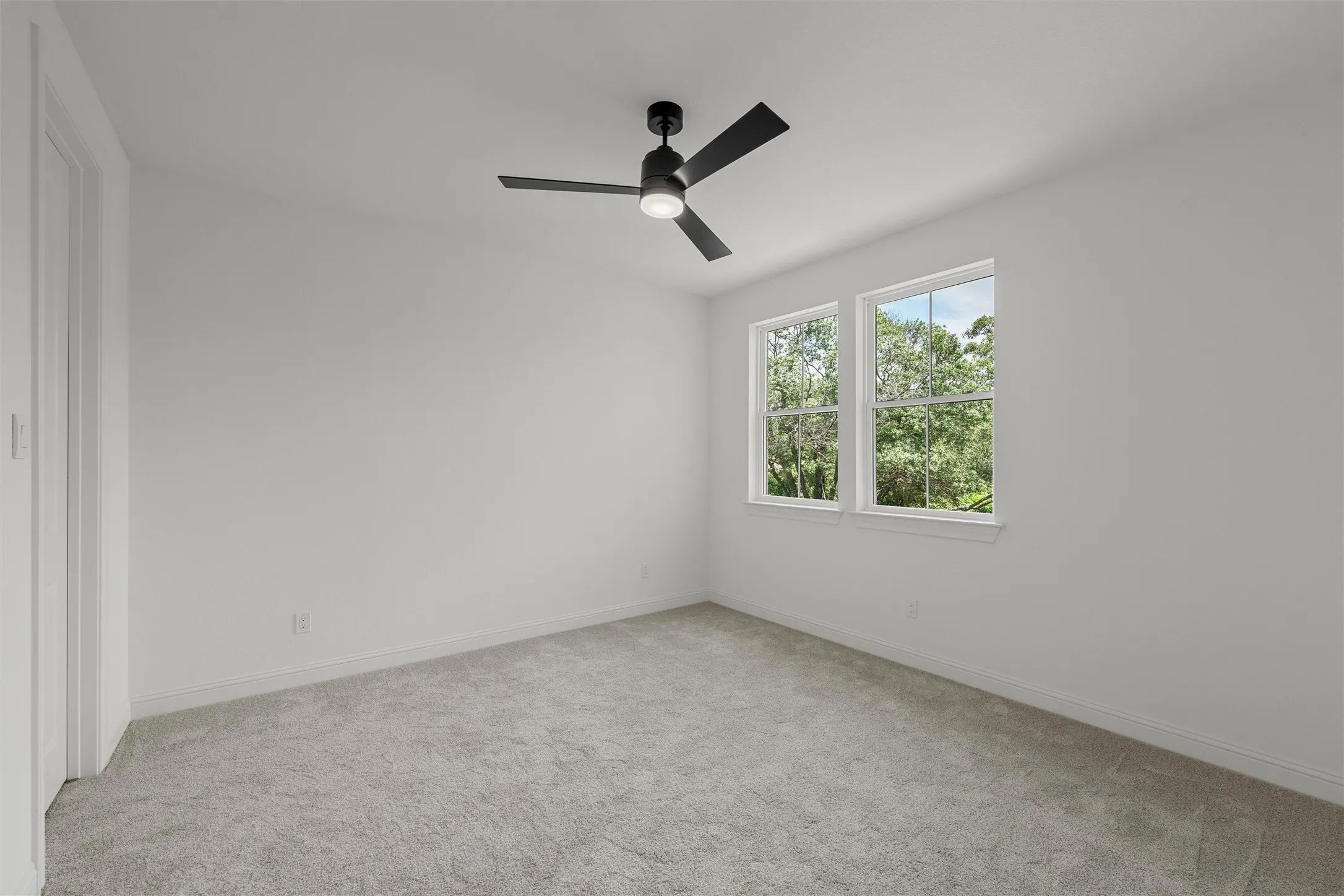 White walls, light gray carpet, and a modern black ceiling fan