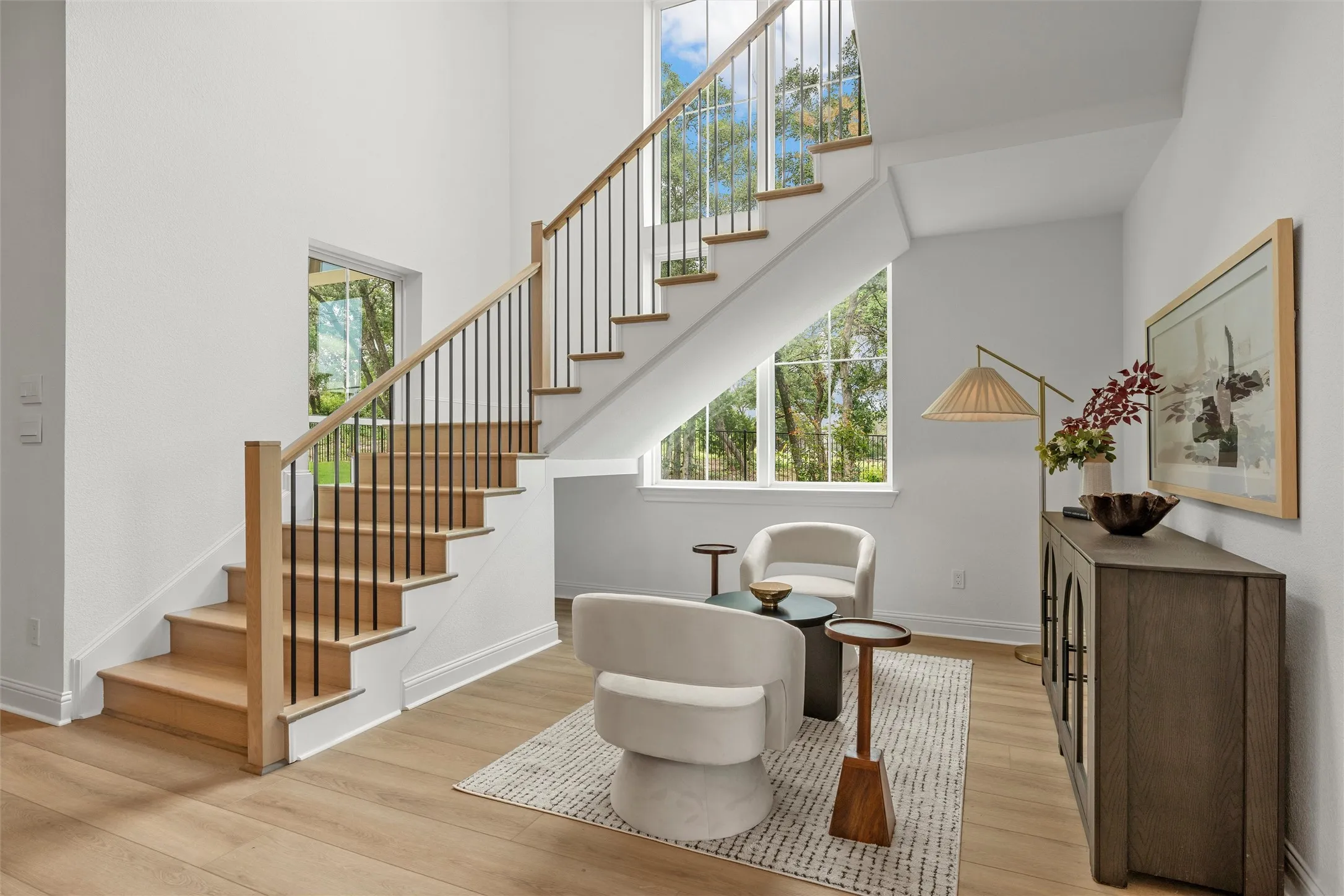 Light wood-finish flooring, two-story ceilings, a staircase with wood treads and balusters, and expansive windows