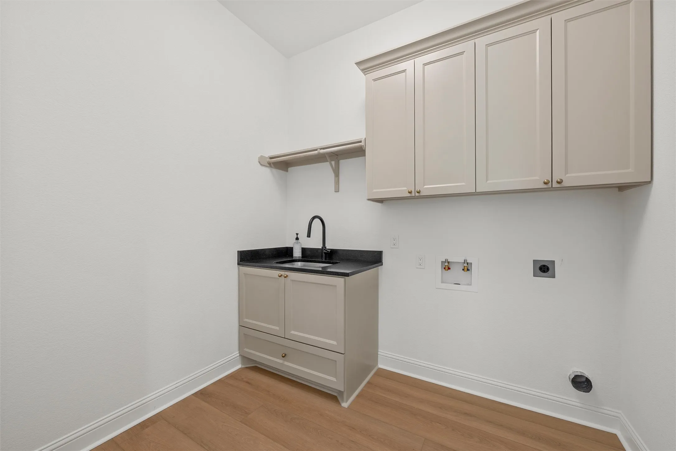 Laundry area featuring wood-finish flooring, built-in cabinetry, a utility sink with a matte black faucet, and a wall-mounted shelving unit