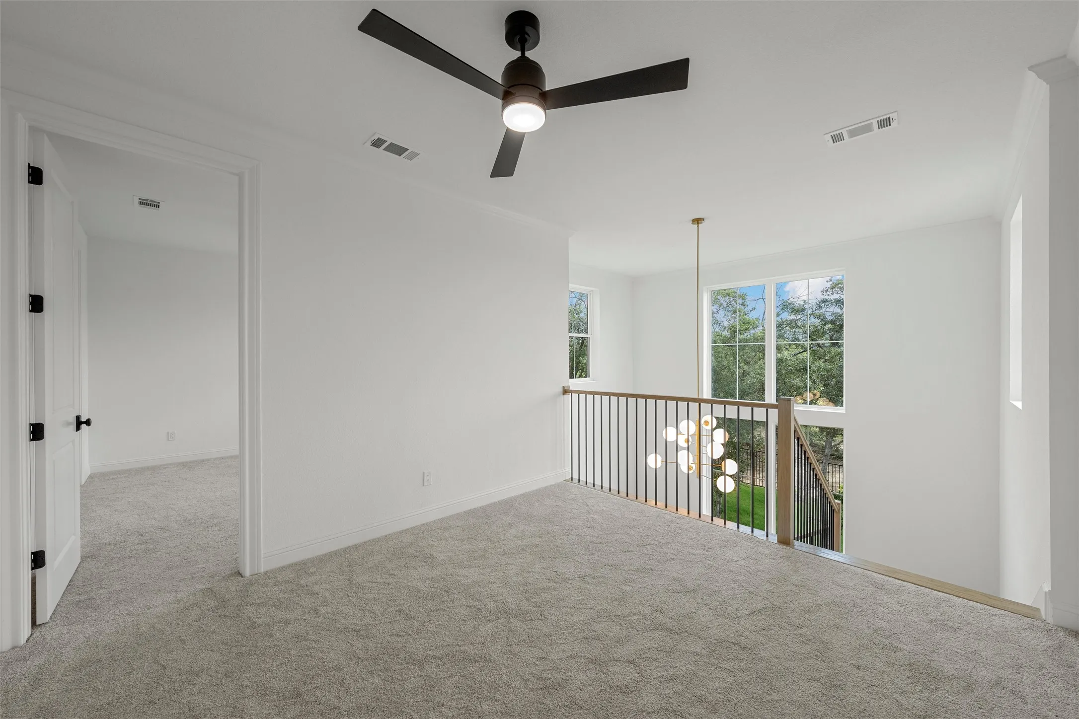 Carpeted landing with white walls, contemporary ceiling fan, and black metal railing