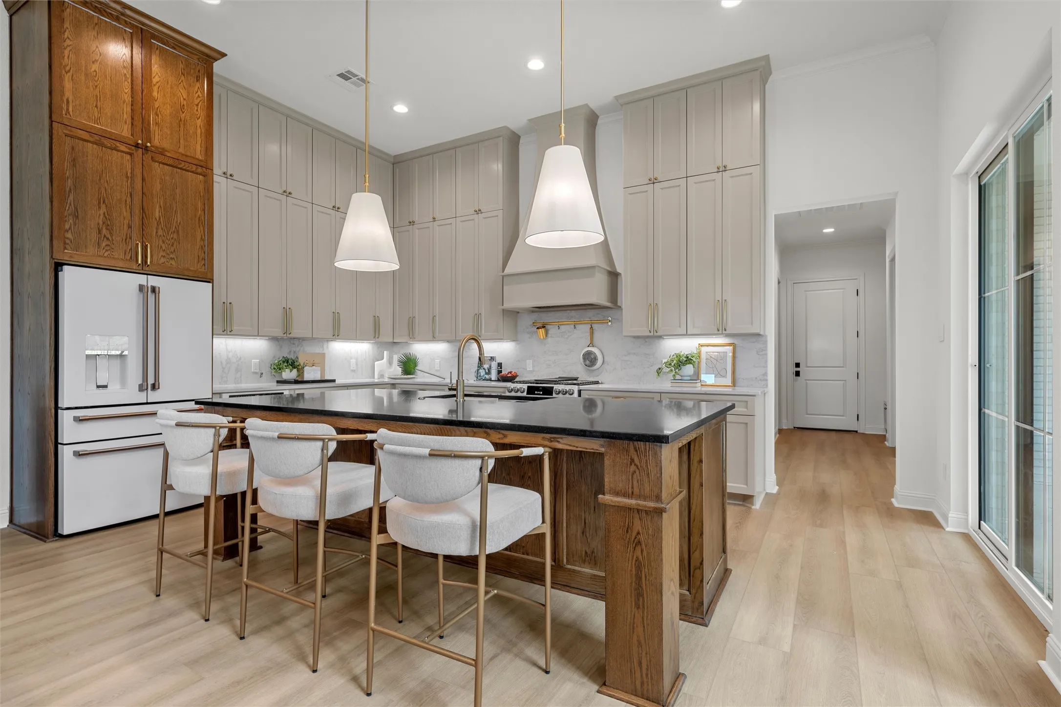 Kitchen featuring an expansive island with a dark countertop, light wood-finish flooring, two large pendant lights, and a full suite of white appliances