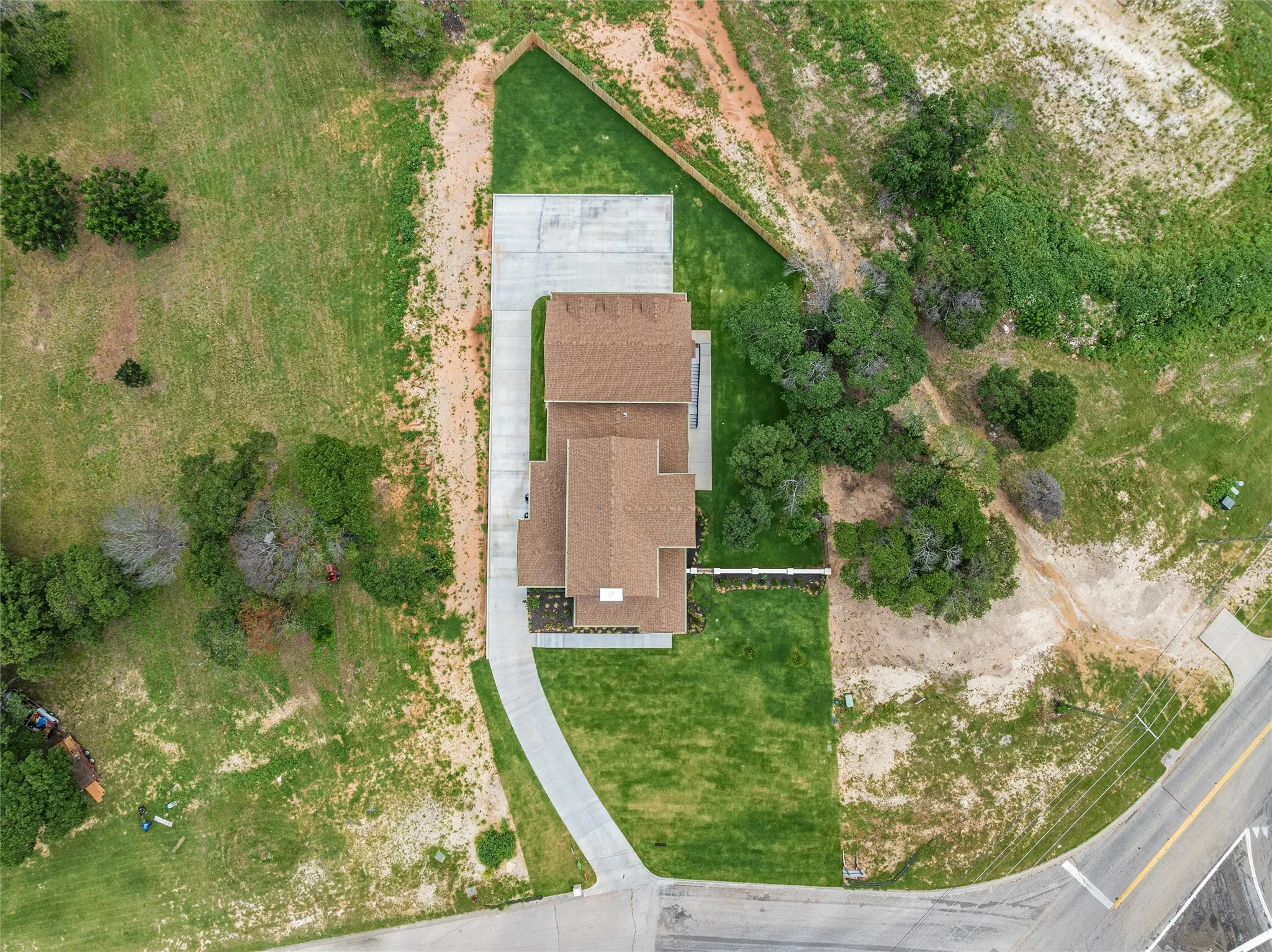 Expansive parcel featuring a newly constructed residence with a brown shingle roof, a concrete driveway, and established green lawns