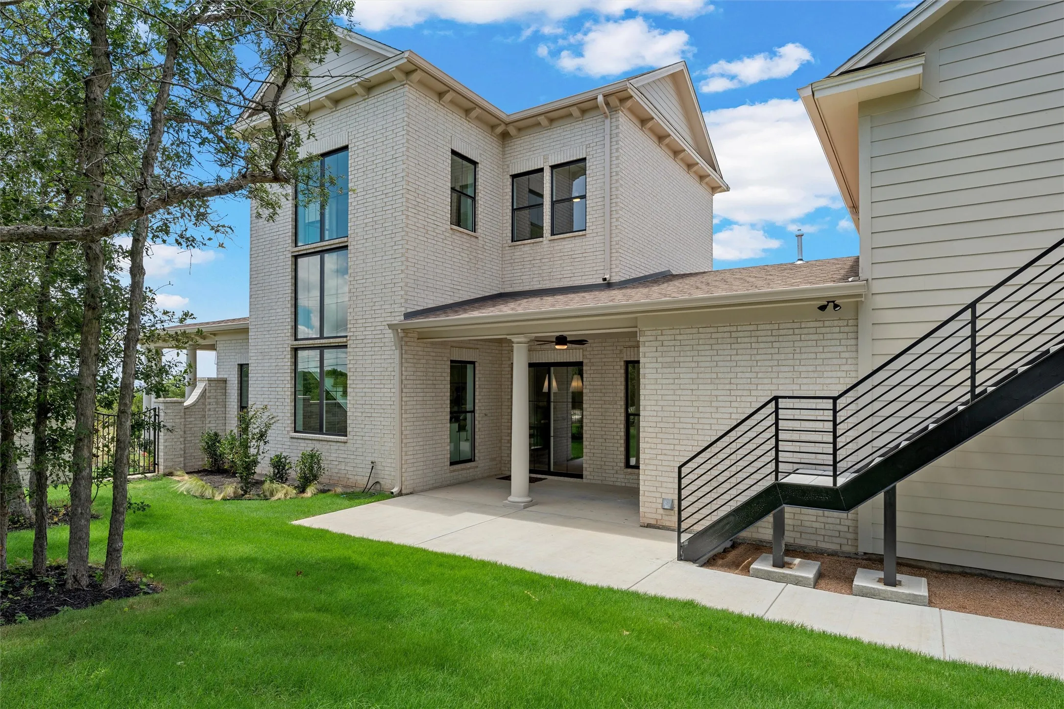 White brick exterior with a covered patio, black framed windows, and a metal outdoor staircase