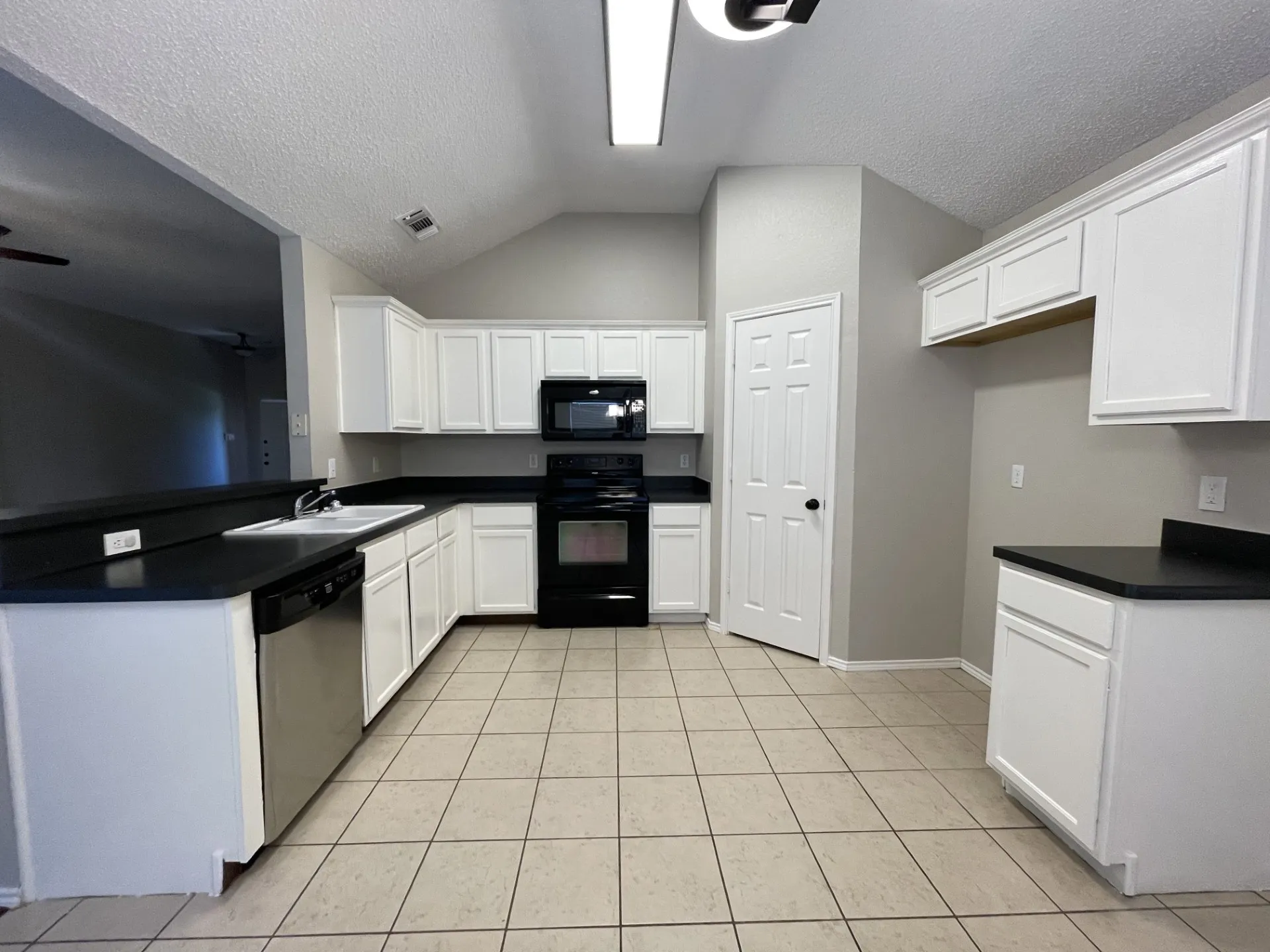 Kitchen with black appliances, dark countertops, light tile patterned flooring, vaulted ceiling, and white cabinetry