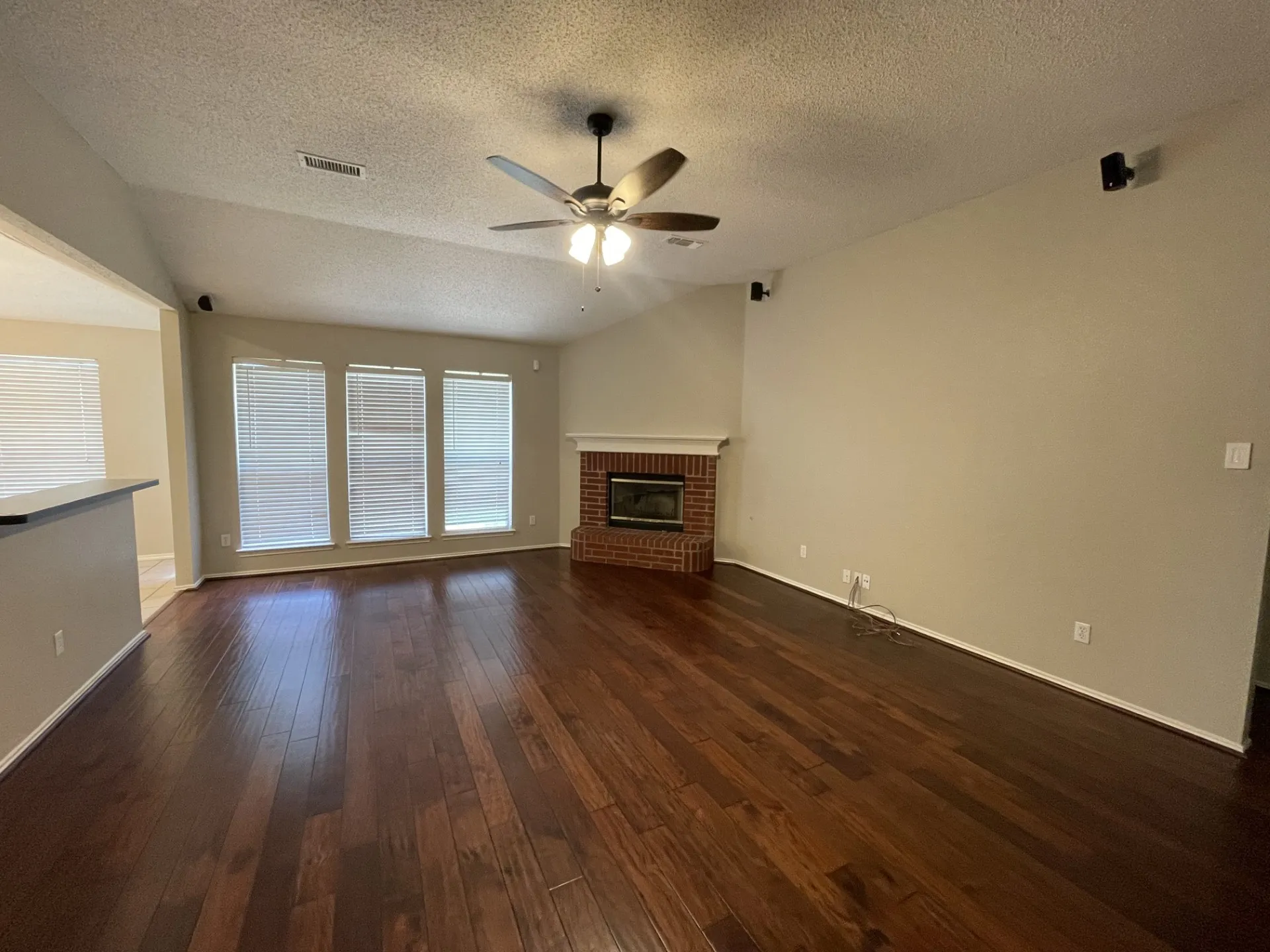 Unfurnished living room featuring ceiling fan, dark wood-type flooring, a textured ceiling, and a brick fireplace