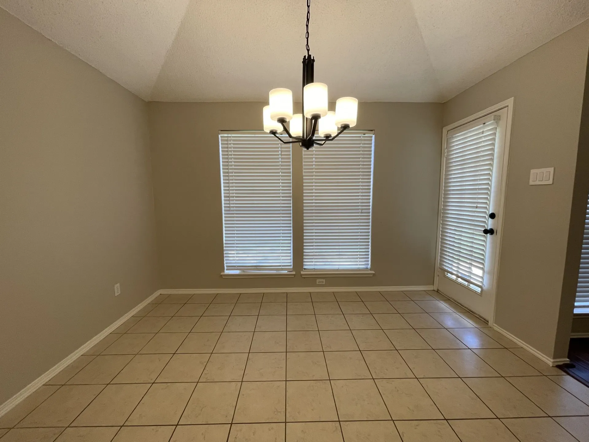 Empty room with a chandelier, light tile patterned floors, a textured ceiling, and lofted ceiling