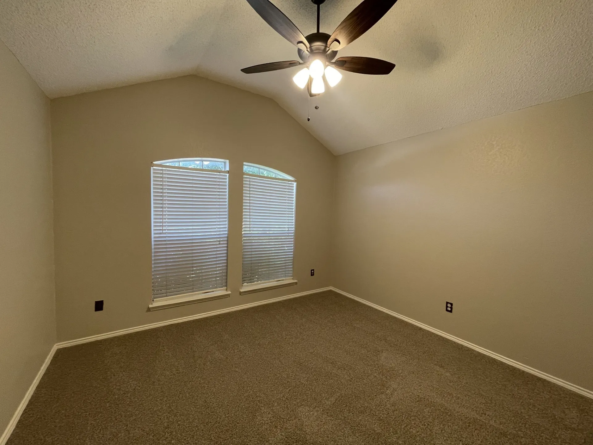 Empty room with vaulted ceiling, a ceiling fan, dark carpet, and a textured ceiling