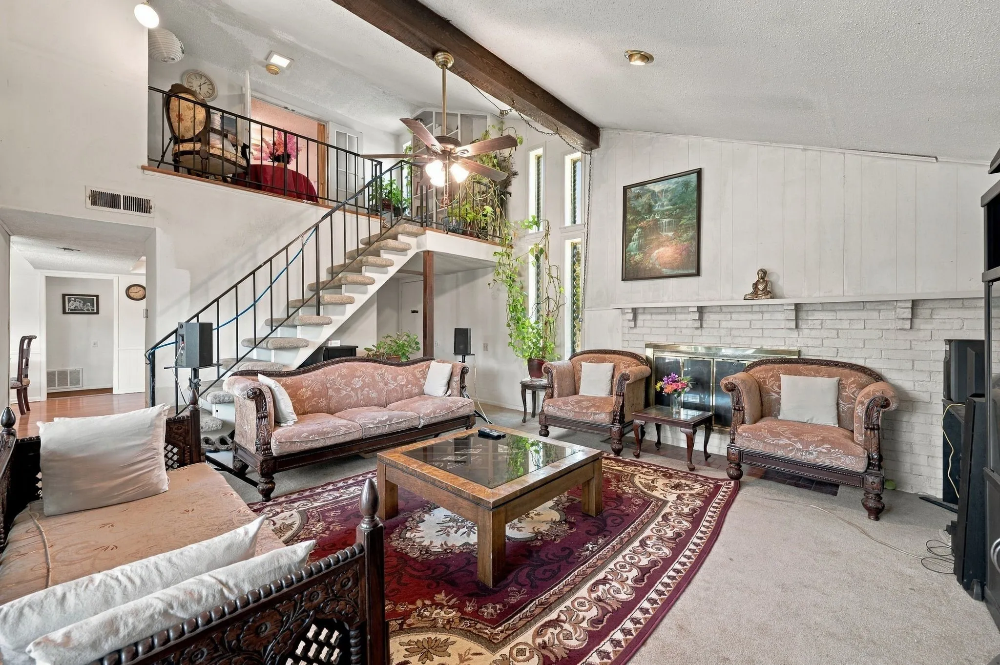 Living room located immediately to the left upon entry from the front door with ceiling fan, and lots of natural light, and half-wall brick fireplace with gas starter. This view shows the front entry and the stairway to the upstairs.