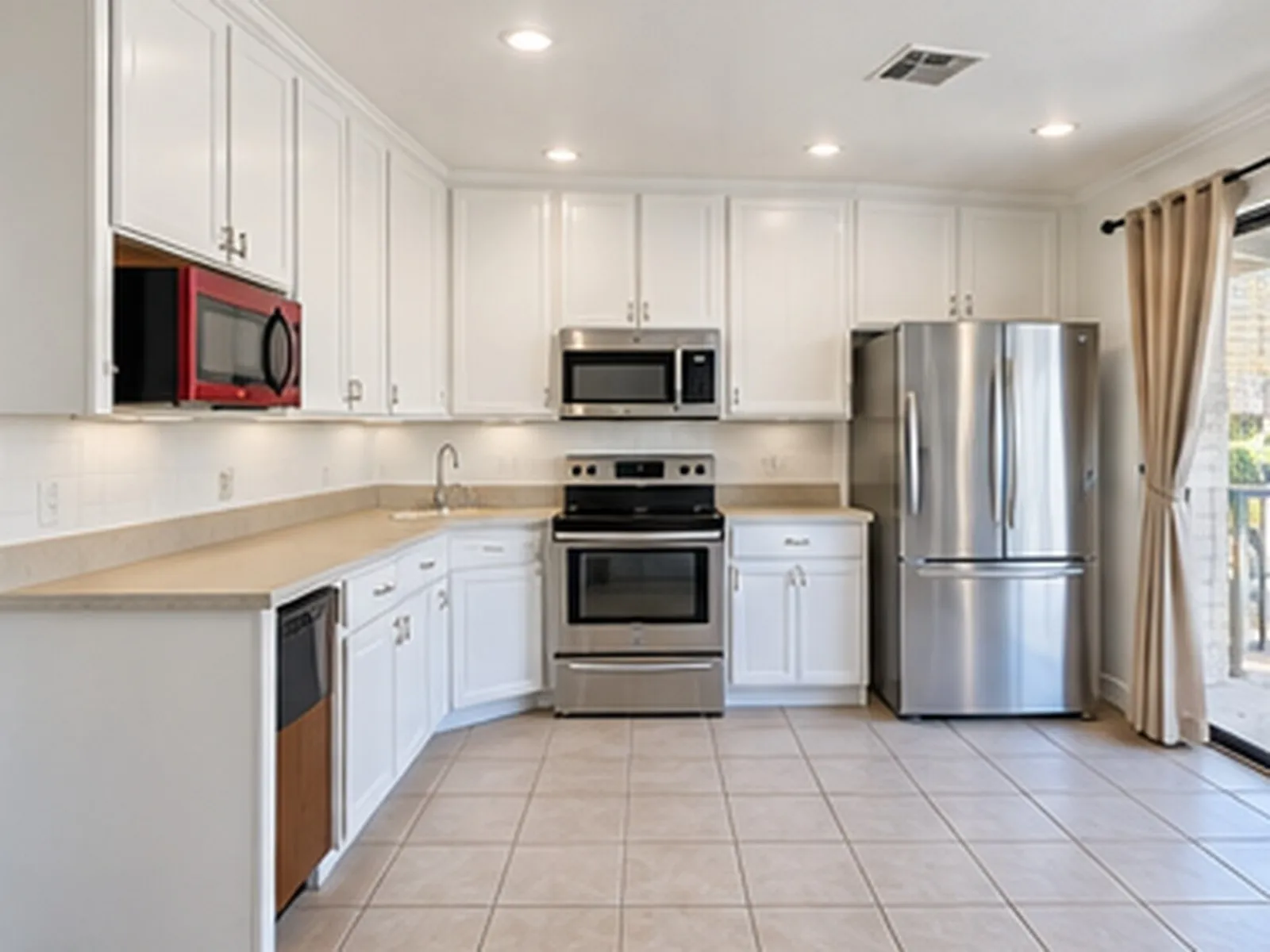 White cabinetry, stainless steel appliances, recessed ceiling lights, tile flooring, and a sliding glass door