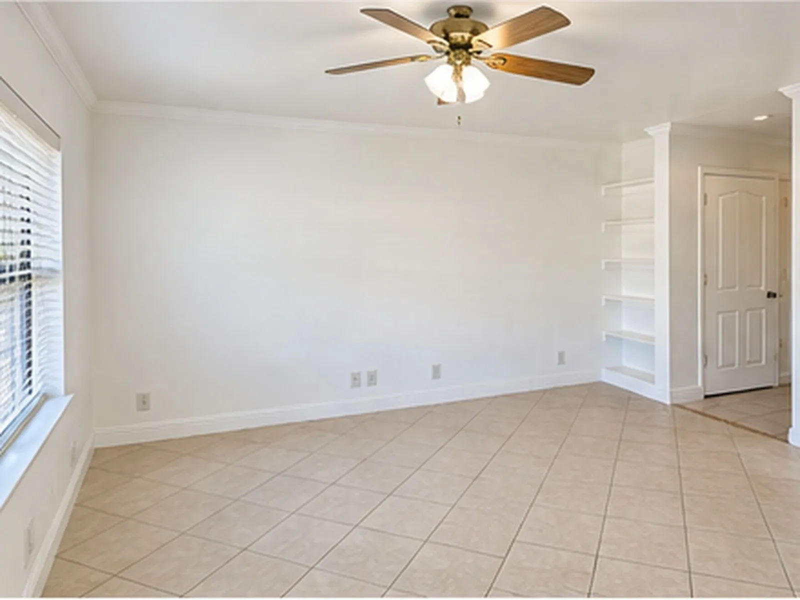 Recessed built-in shelving, ceiling fan with light fixture, large window with blinds, crown molding, and tile flooring