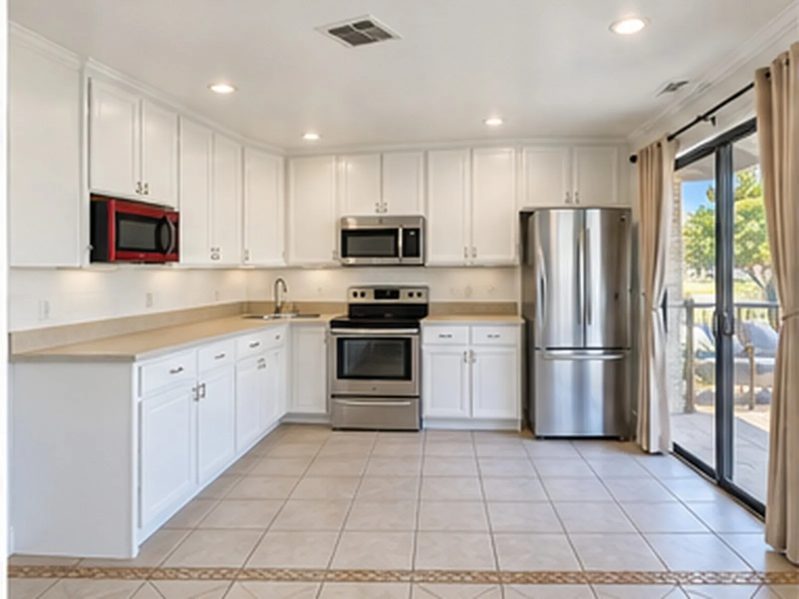 White cabinetry with crown molding, stainless steel appliances, recessed lighting, and a sliding glass door leading to an outdoor deck
