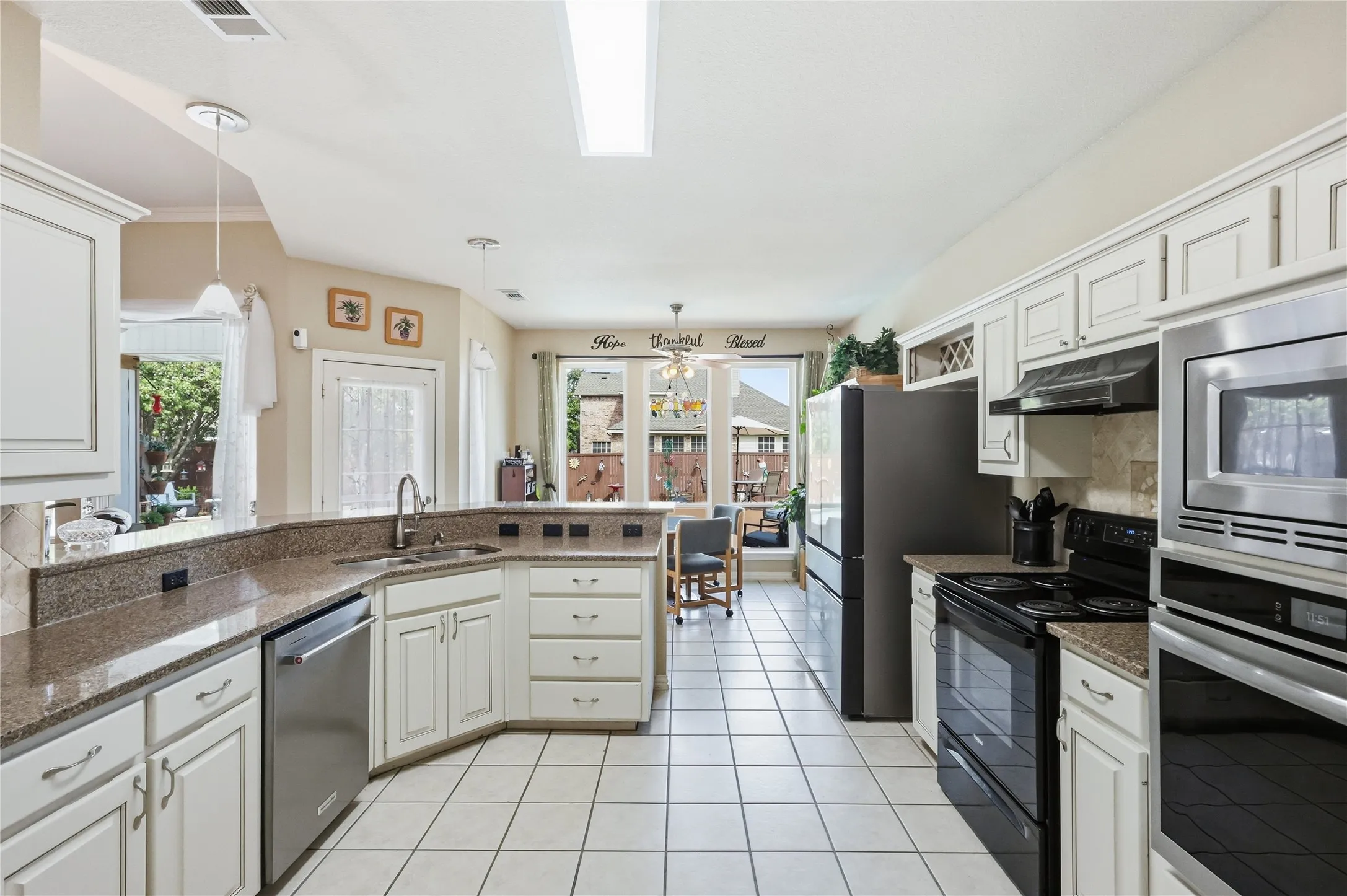 White cabinetry with brushed nickel hardware, granite-look countertops, stainless steel appliances, tiled flooring, and ample natural light