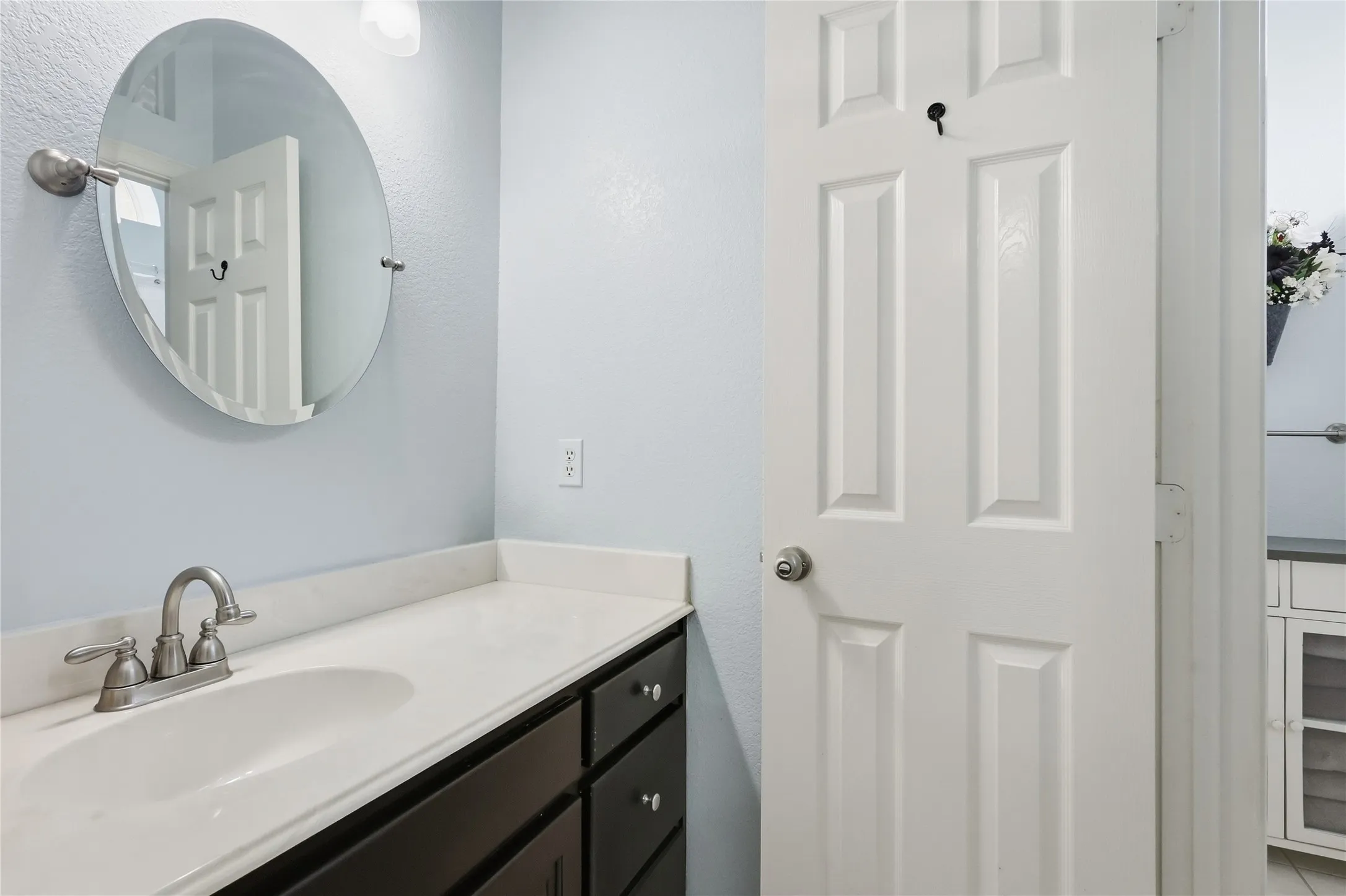 Vanity with an integrated sink, brushed nickel faucet, dark wood-finish cabinetry, and a round wall-mounted mirror
