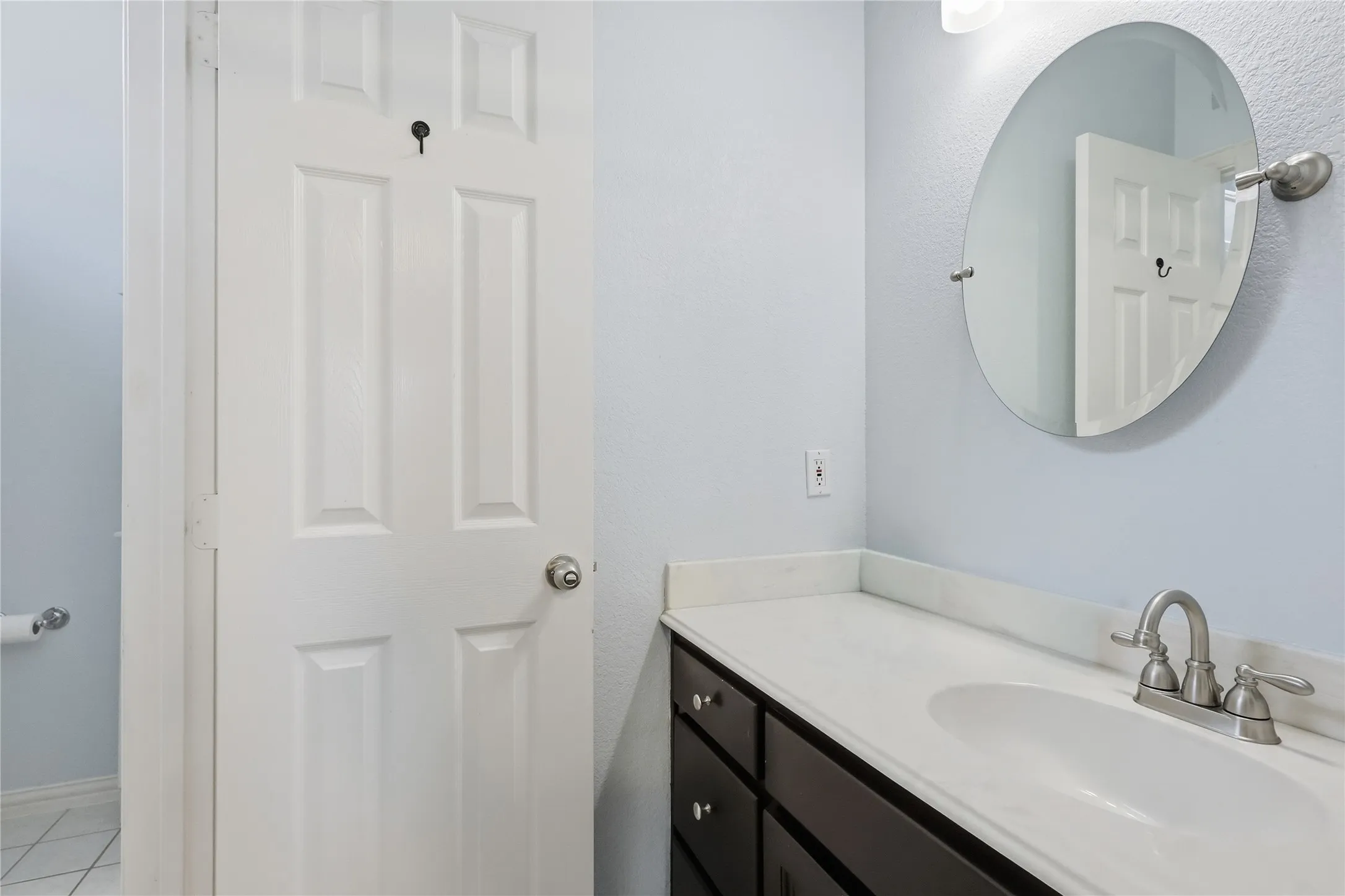 White countertop with integrated sink, dark wood-finish vanity, brushed nickel faucet, and oval wall-mounted mirror