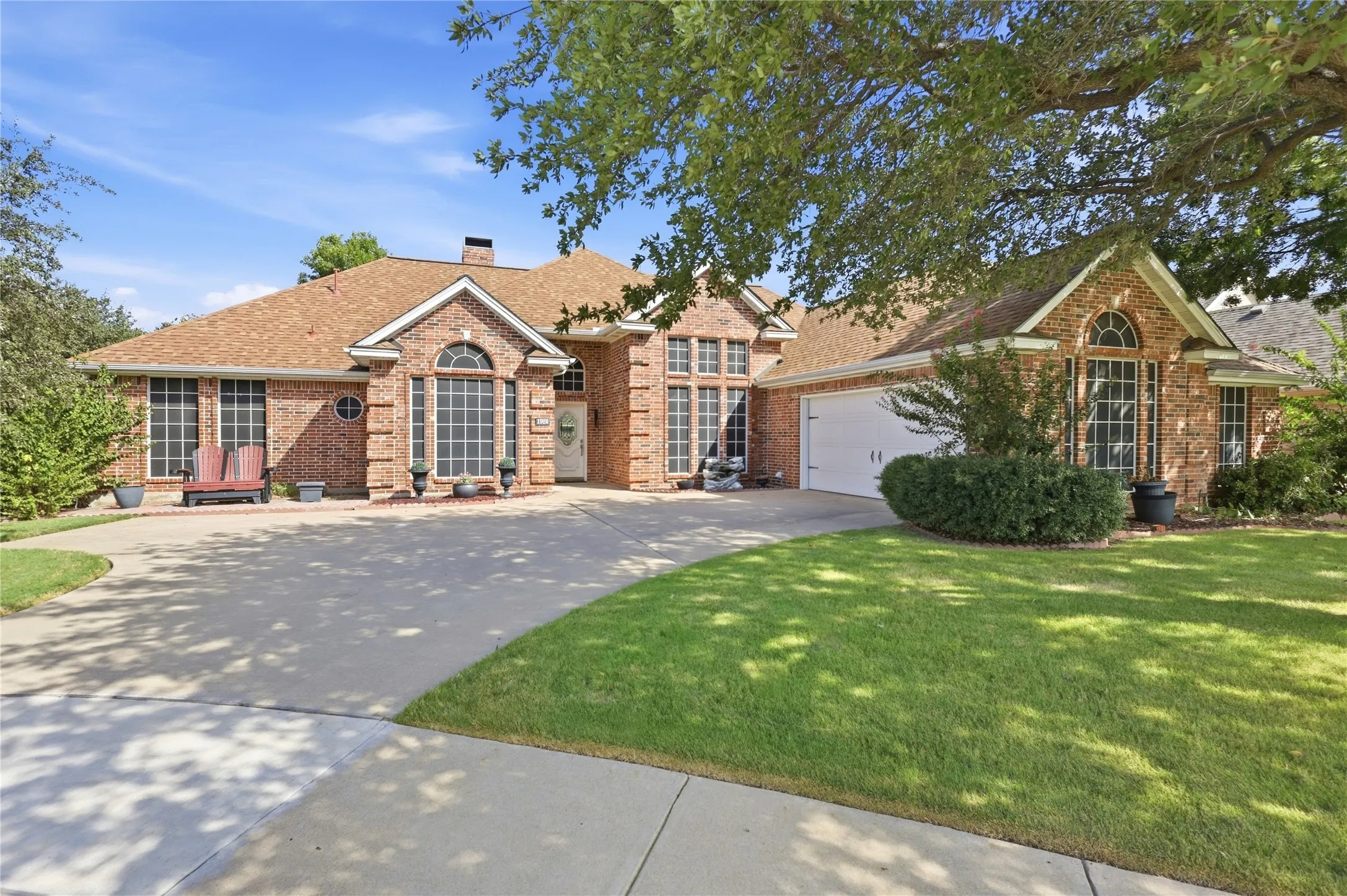Brick exterior with a prominent arched window, multi-paned windows, and a large driveway