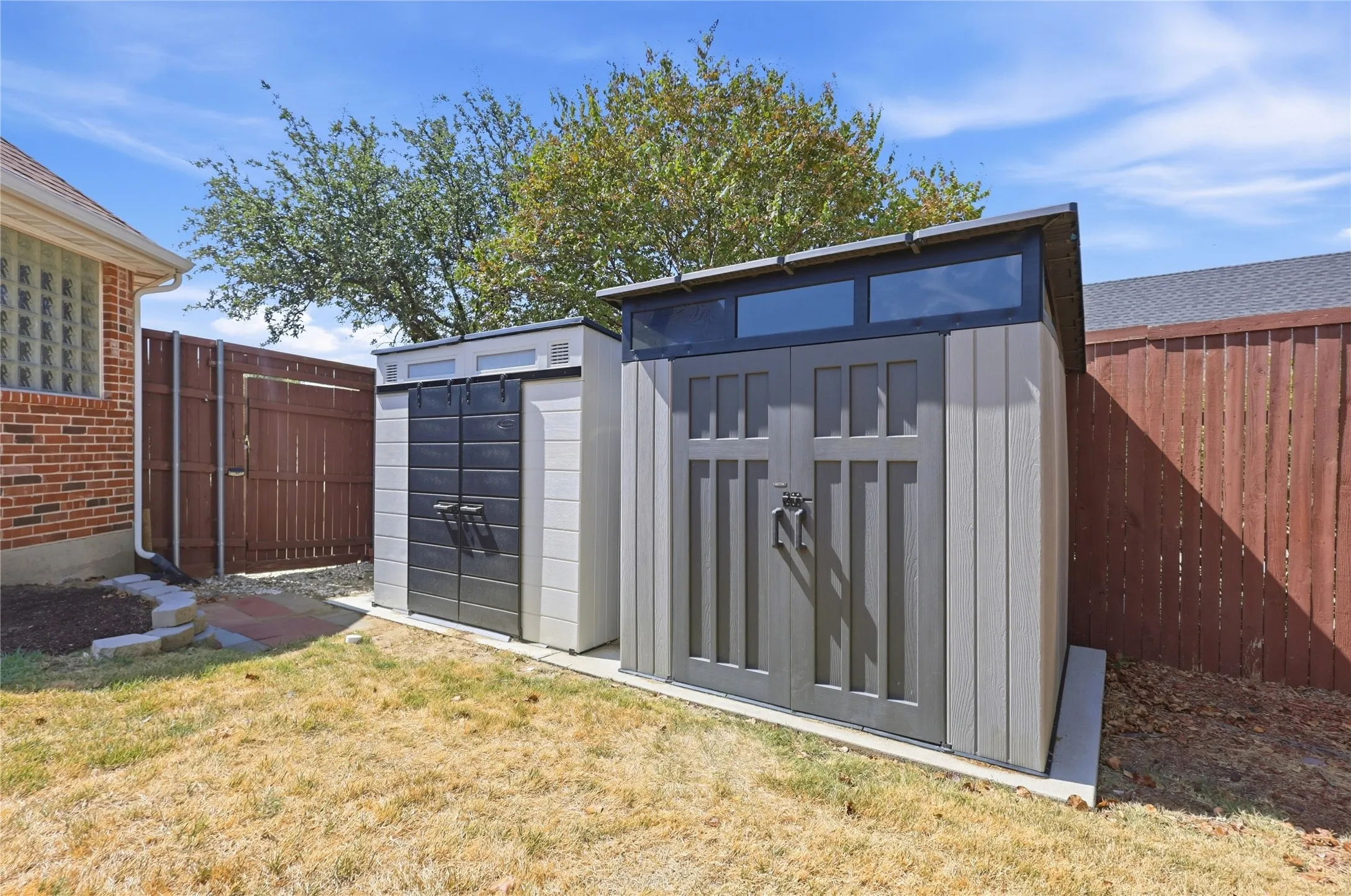 Two storage sheds with a wood-look finish, featuring transom windows and double doors