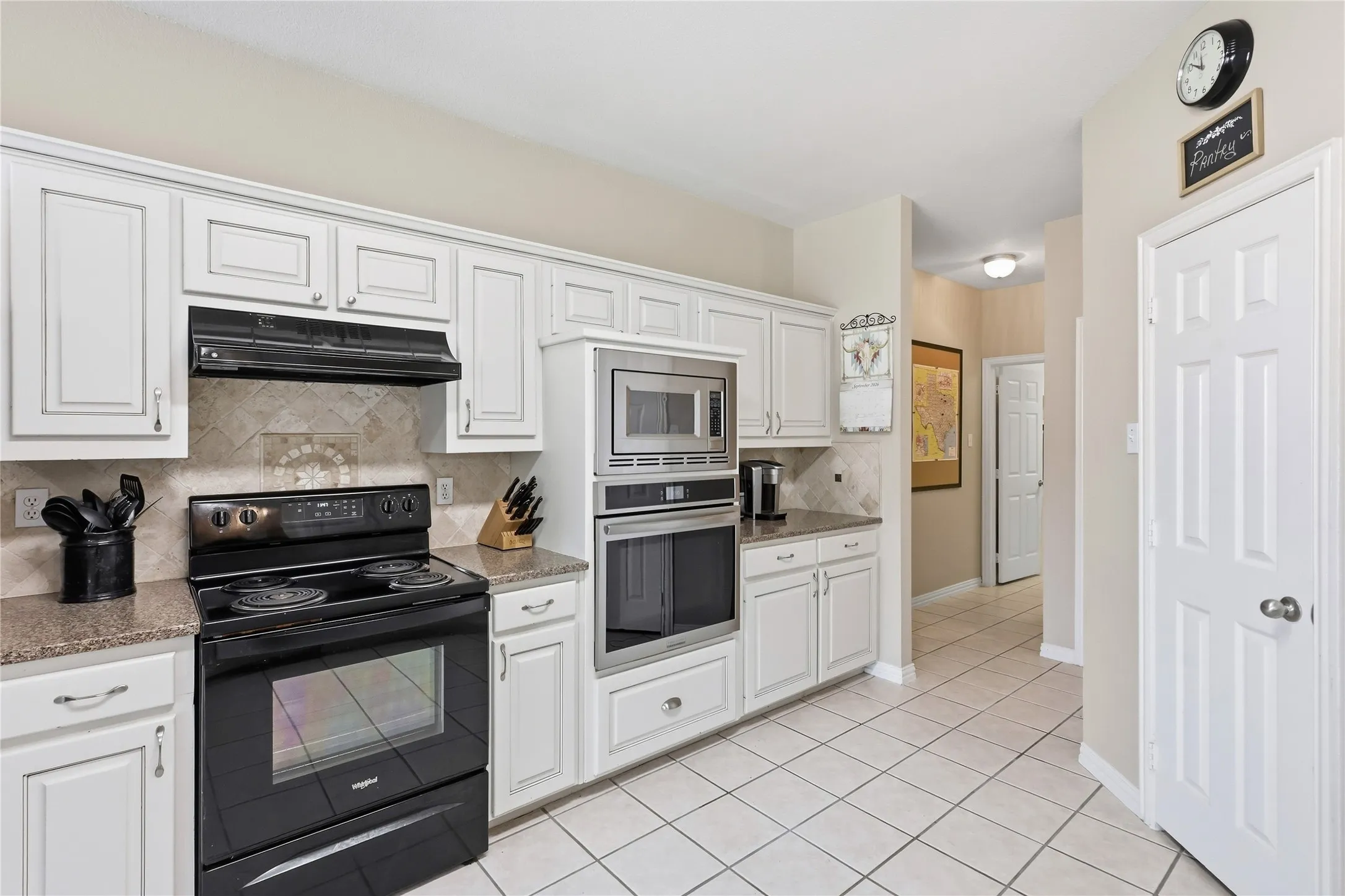 White cabinetry, tile flooring, granite-style countertops, stainless steel microwave, and built-in oven