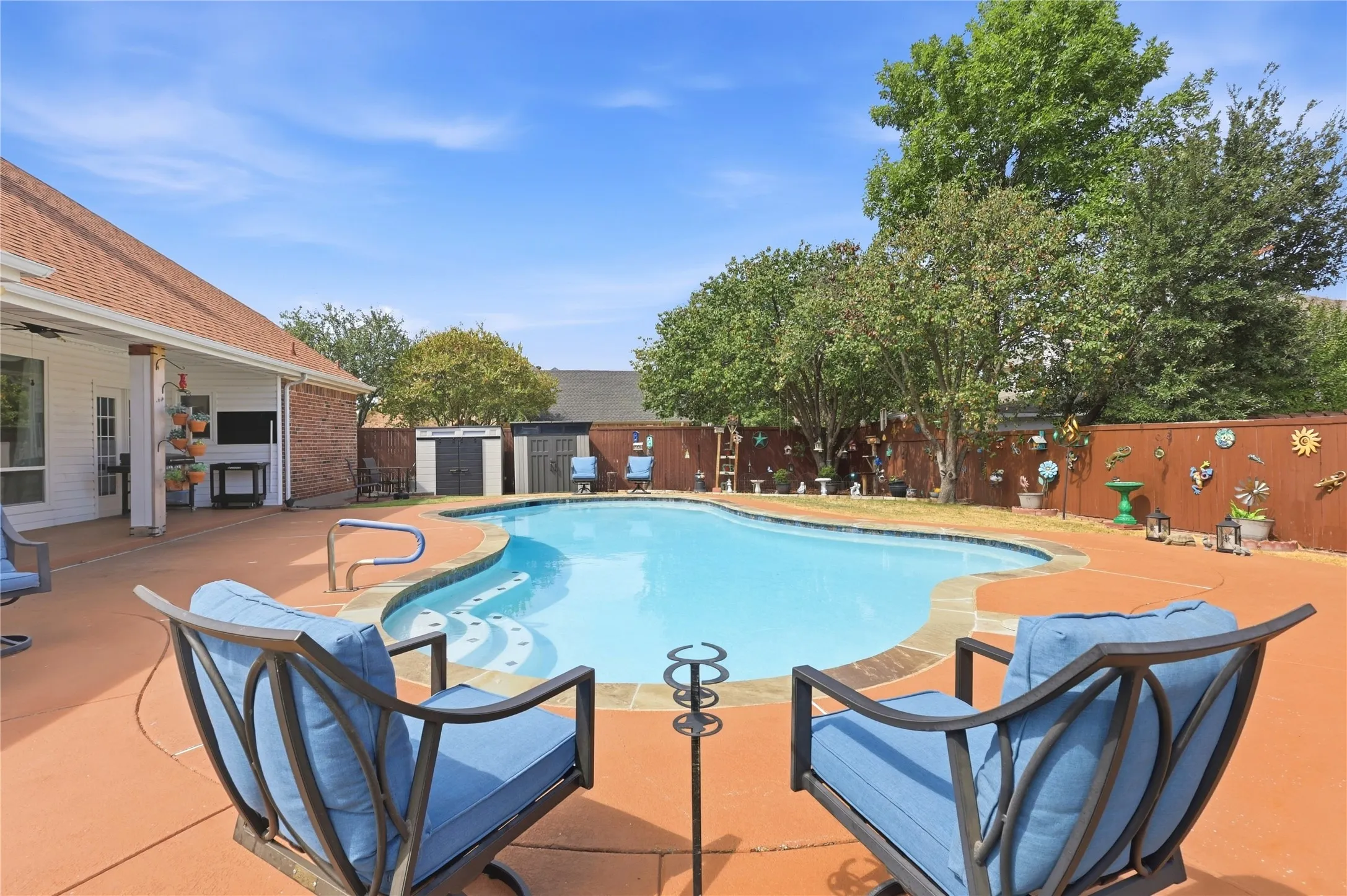 Outdoor swimming pool with integrated steps, surrounded by an expansive concrete patio and a privacy fence