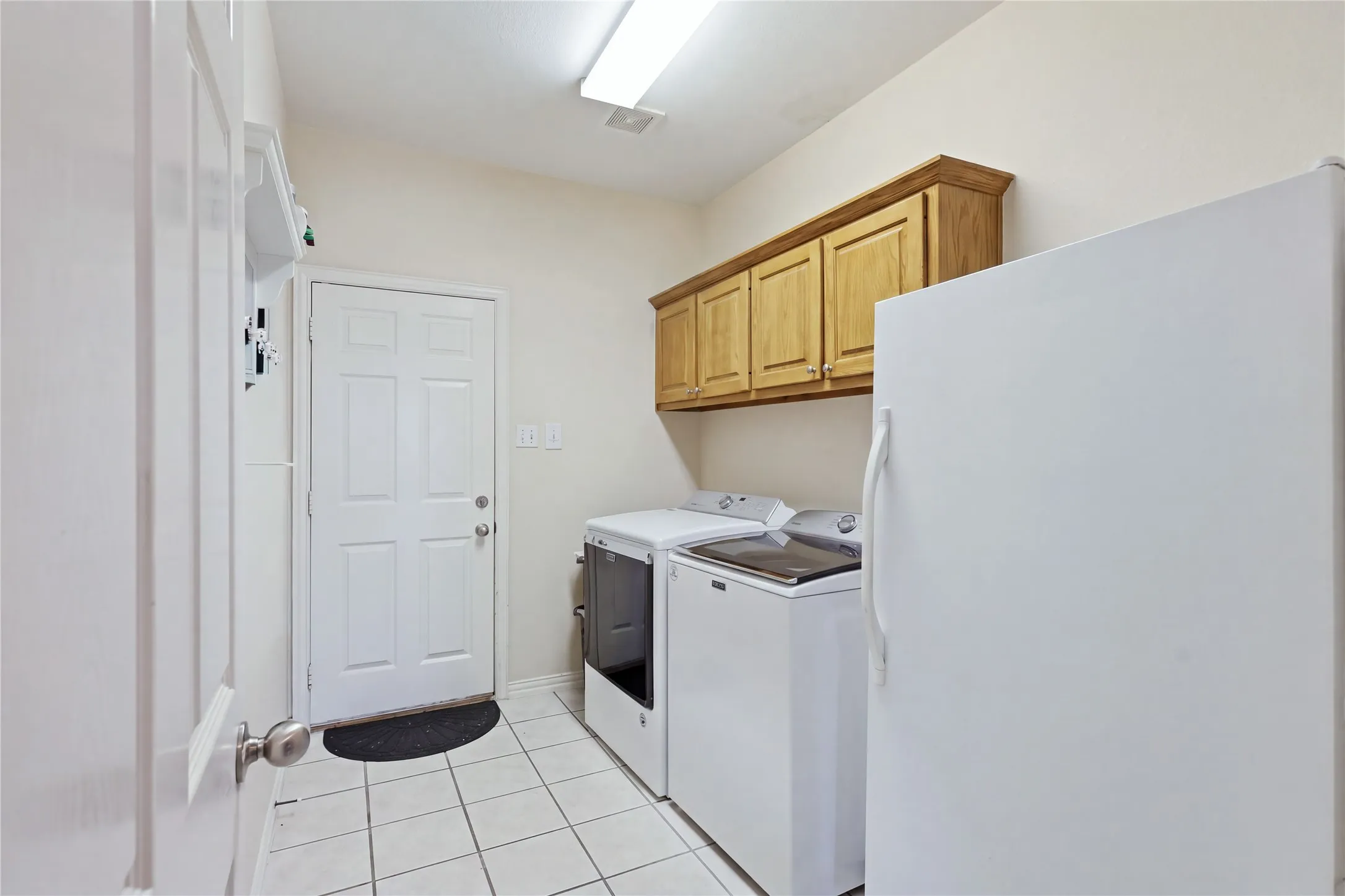 White tile flooring, wood-finish upper cabinetry, and a panel door