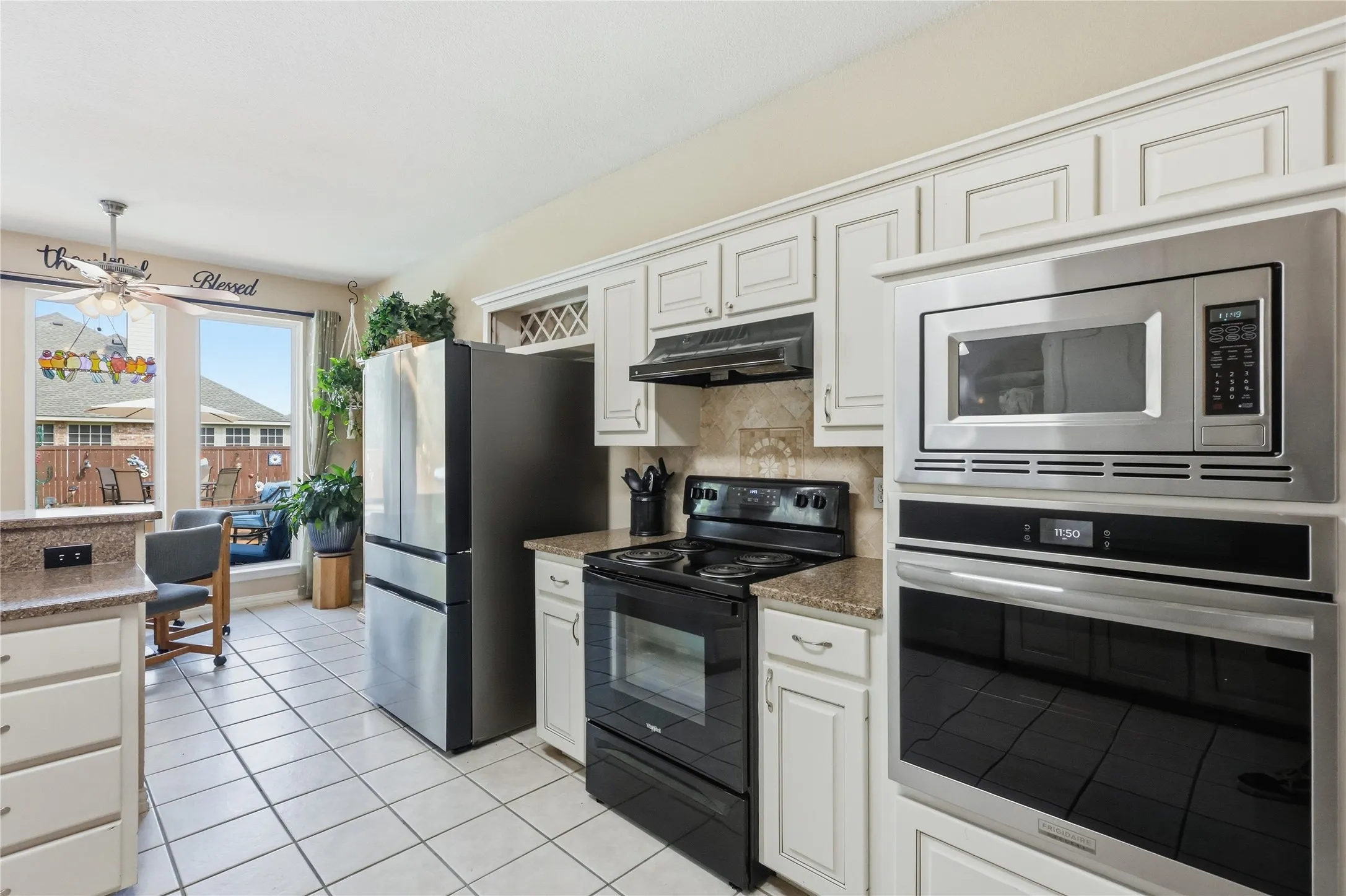 Kitchen with white tile flooring, white cabinetry, integrated stainless steel microwave, black electric range, and light-colored countertops