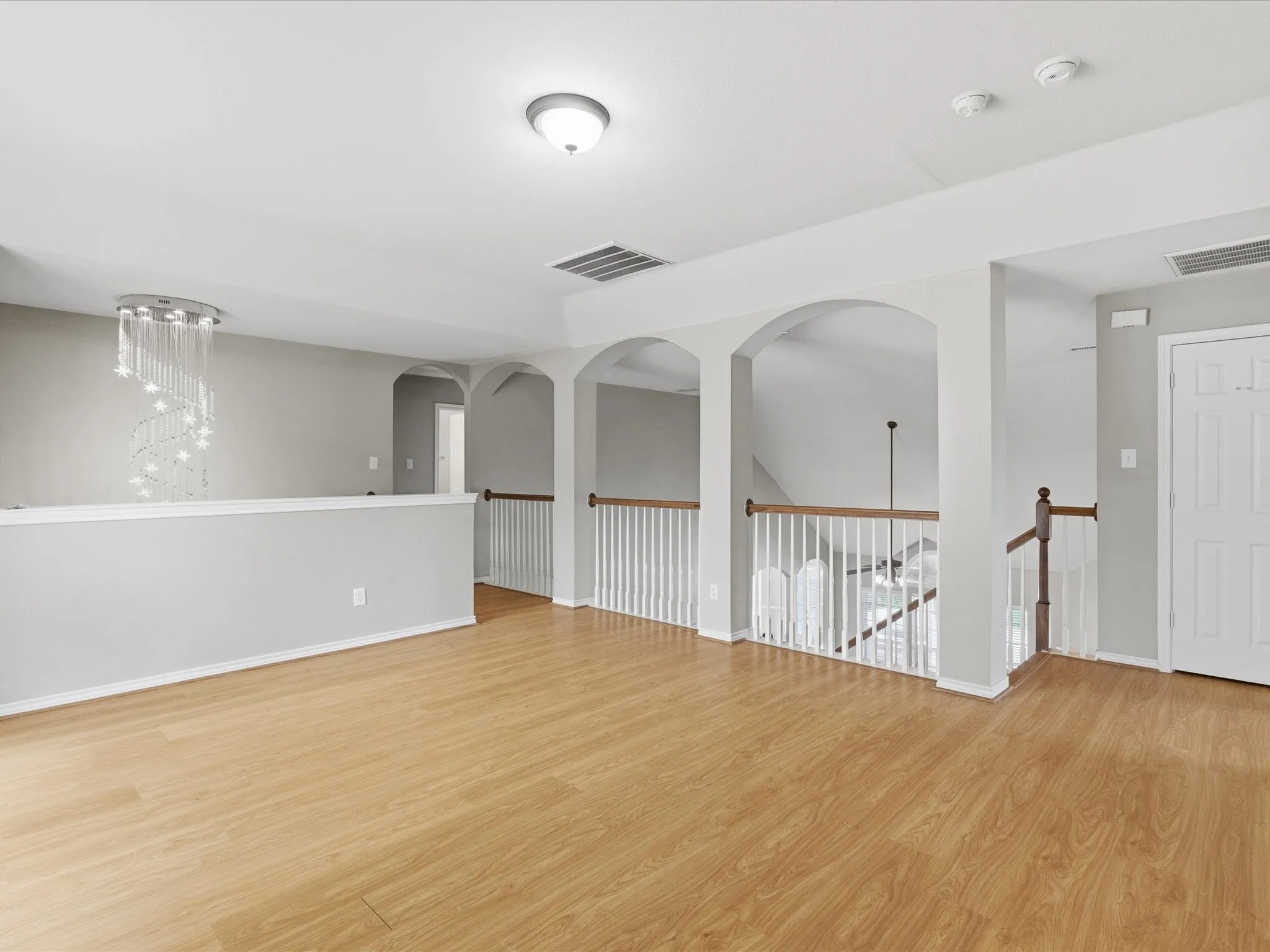 Open common area featuring wood-finish flooring, a contemporary chandelier, and arched doorways