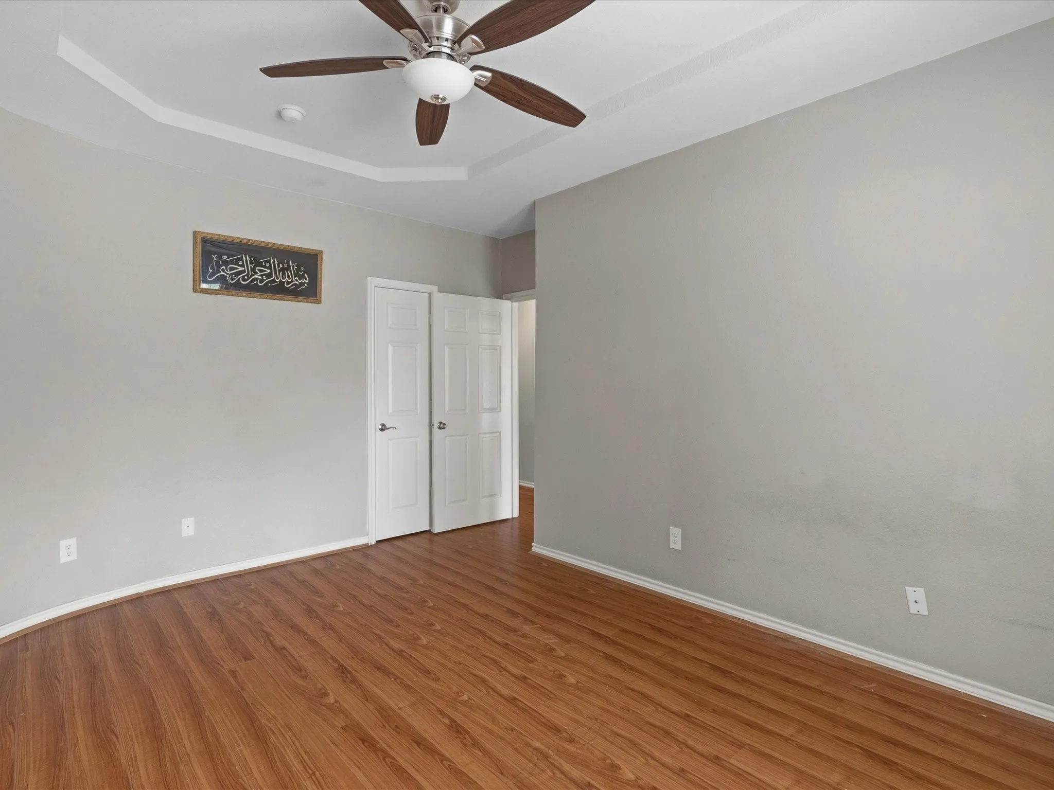 Wood-finish flooring, tray ceiling with ceiling fan, and white paneled doors