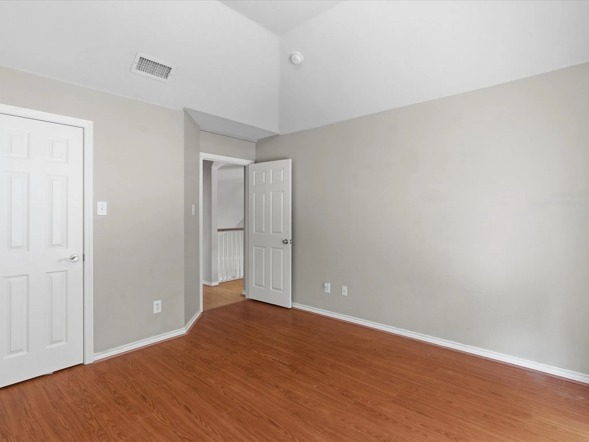 Vaulted ceiling, wood-finish flooring, light gray wall paint, white trim, and white paneled doors