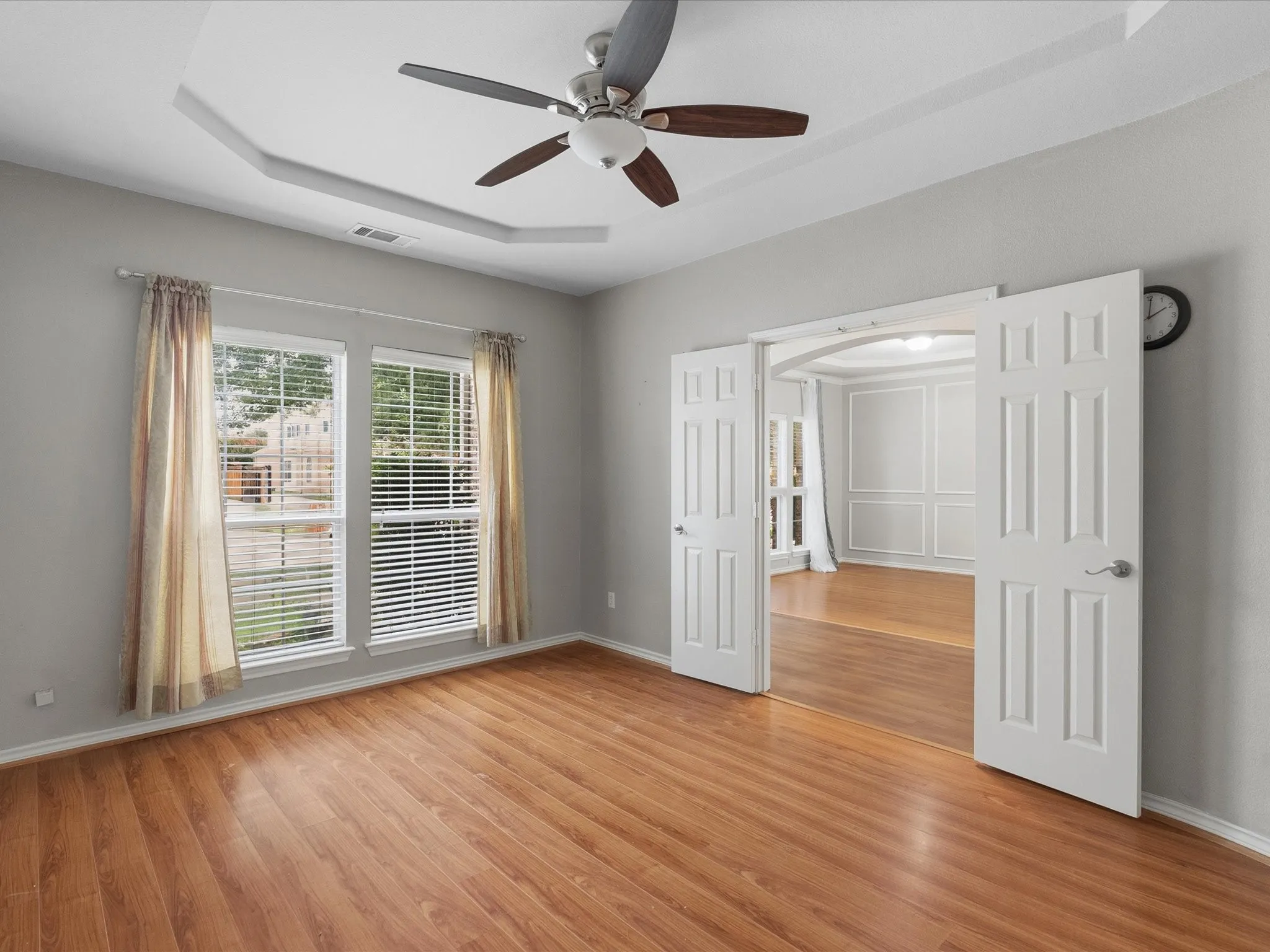 Tray ceiling with a ceiling fan, wood-finish flooring, and double-pane windows with blinds
