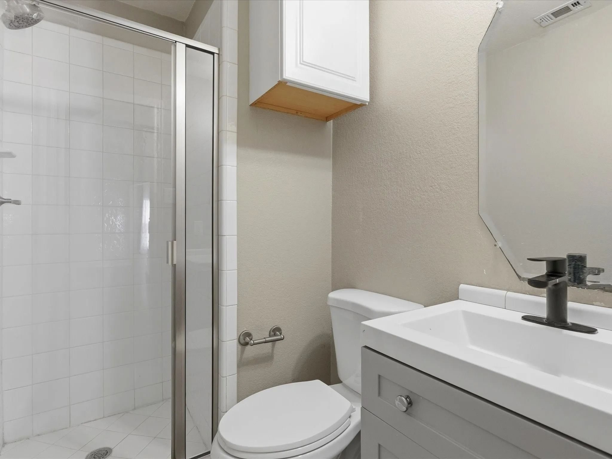 White tile shower with glass enclosure, single vanity with integrated sink, contemporary black faucet, and wall-mounted mirror