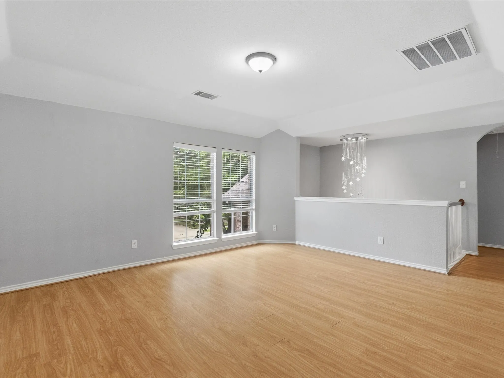Wood-finish flooring throughout, multiple windows with blinds, contemporary chandelier, vaulted ceiling, and a partition wall with a handrail