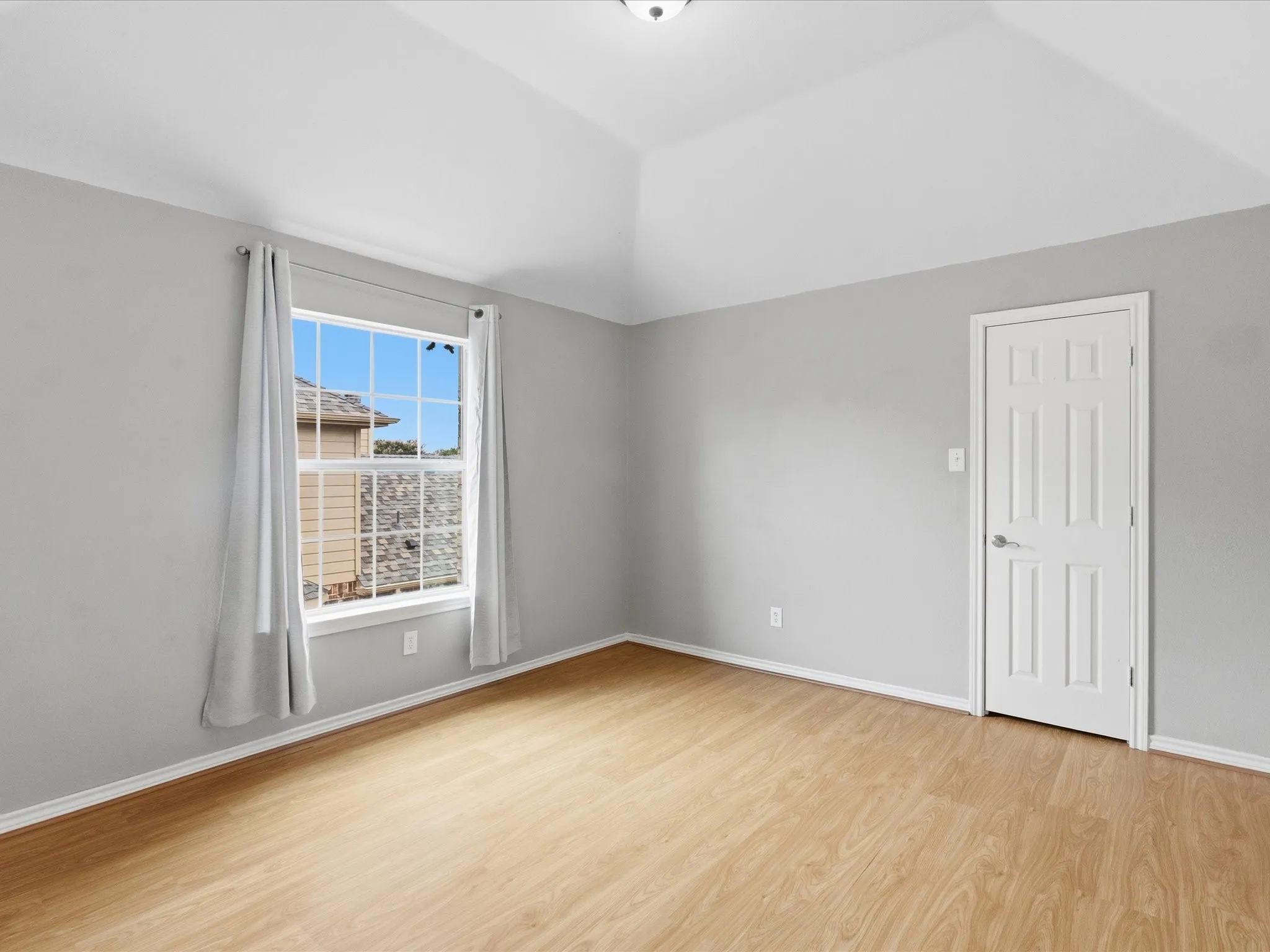 Vaulted ceiling with a flush-mount light fixture, wood-finish flooring, and light gray walls
