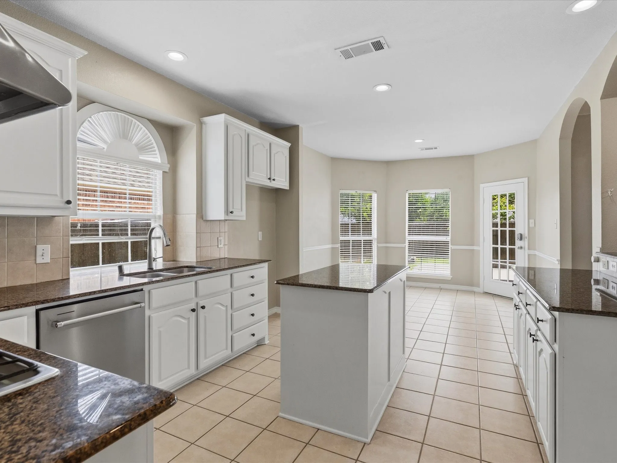 Kitchen featuring an island, white cabinetry, dark stone countertops, tile flooring, and stainless steel appliances
