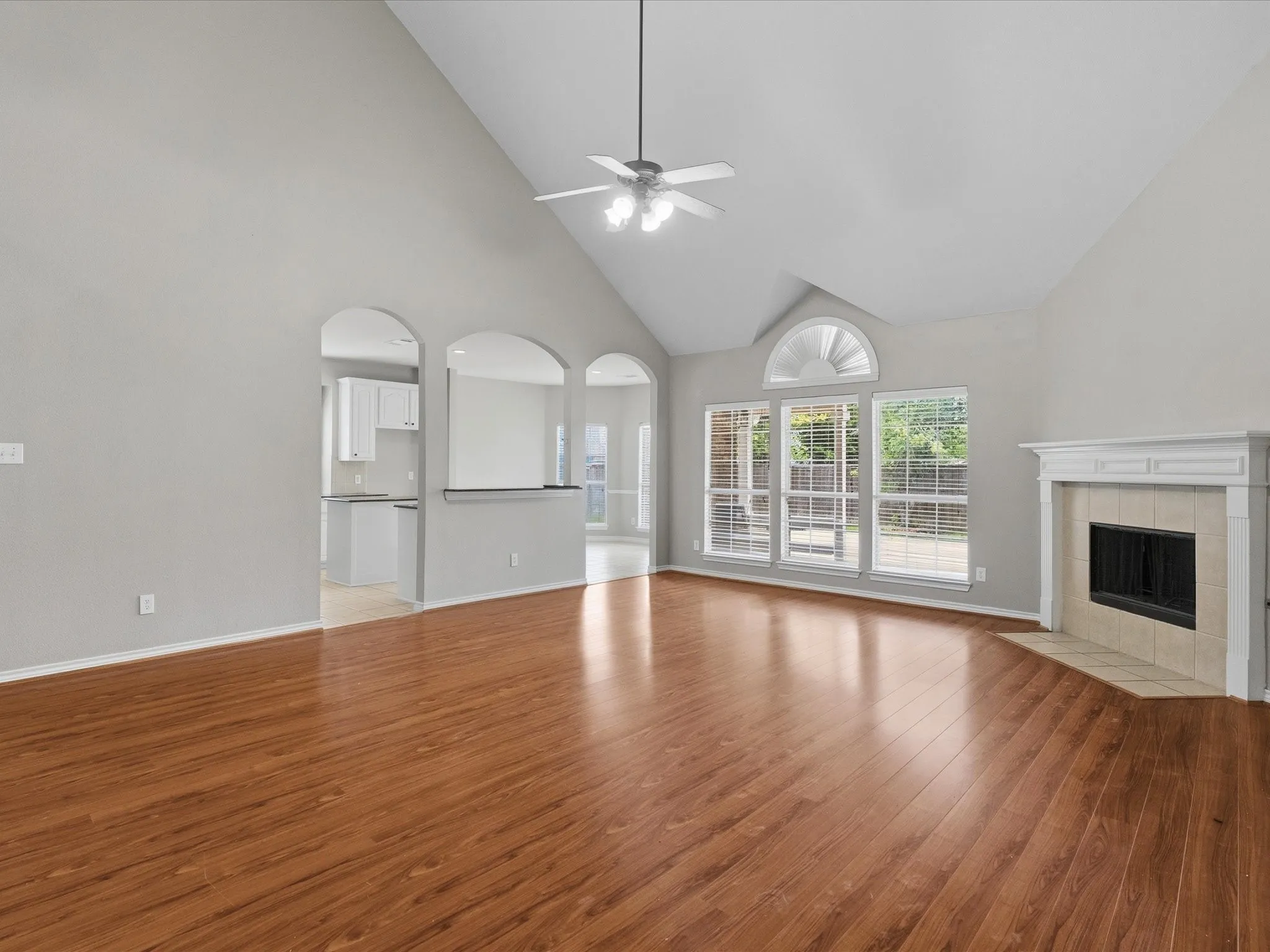 Vaulted ceiling with a ceiling fan, wood-finish flooring, fireplace with a mantel, and arched pass-throughs