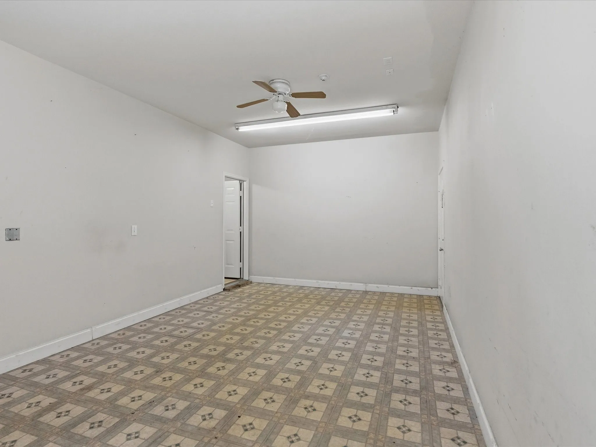 Ceiling fan, fluorescent lighting, patterned floor tiles, white walls, and white trim