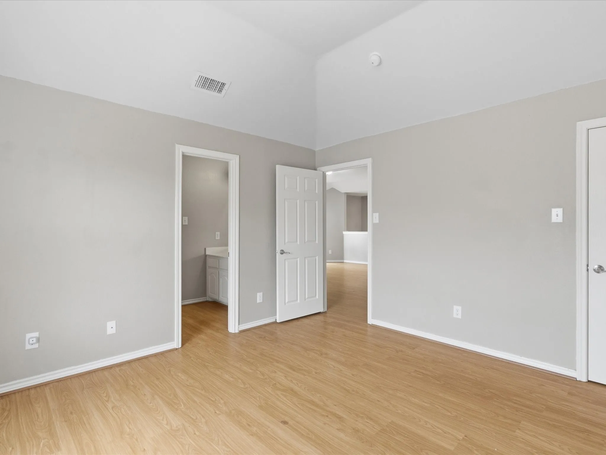 Vaulted ceiling, light wood-finish flooring, neutral wall paint, white trim, and white paneled doors