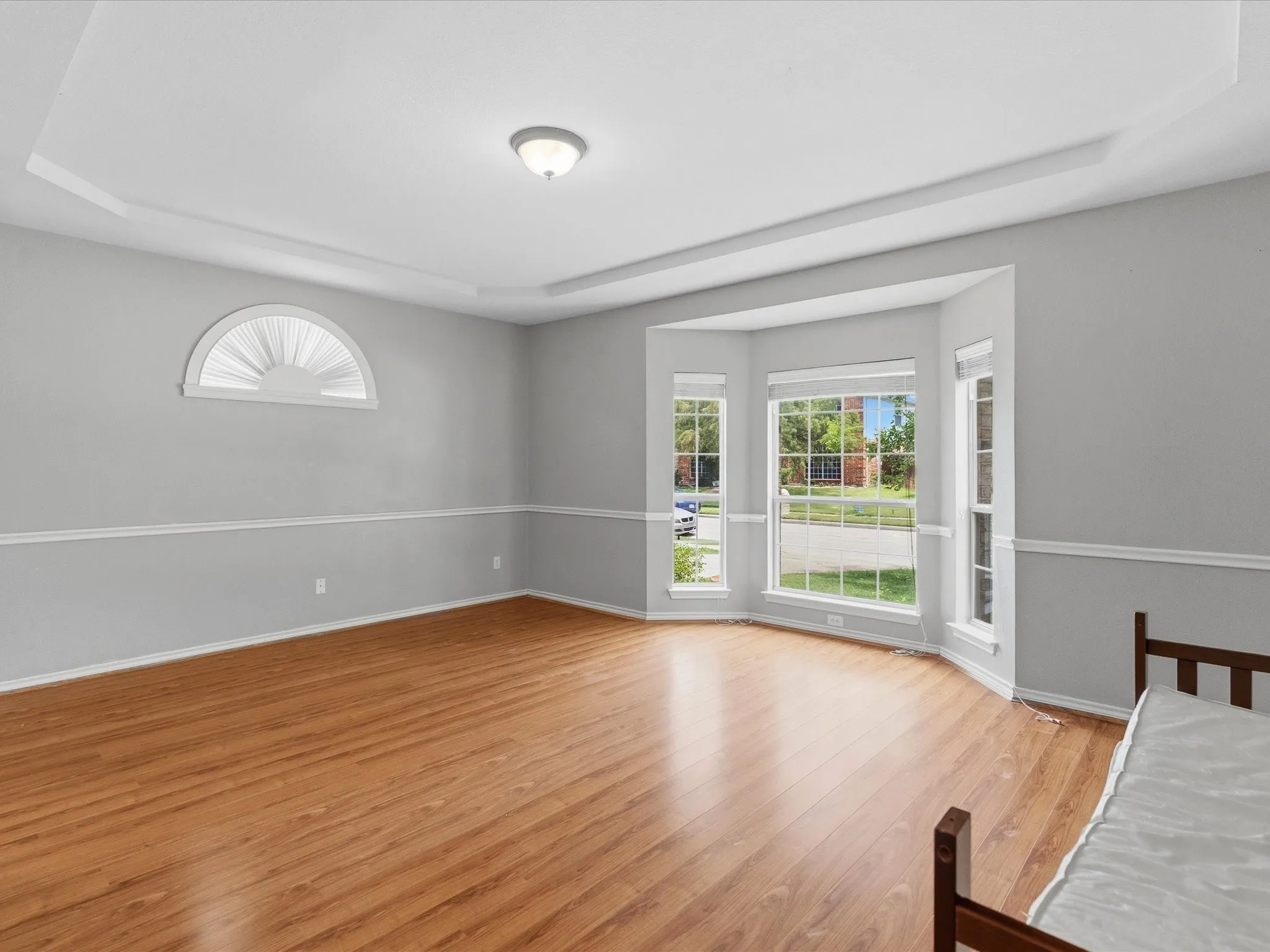 Tray ceiling with recessed lighting, wood-finish flooring, half-round architectural window, and bay windows