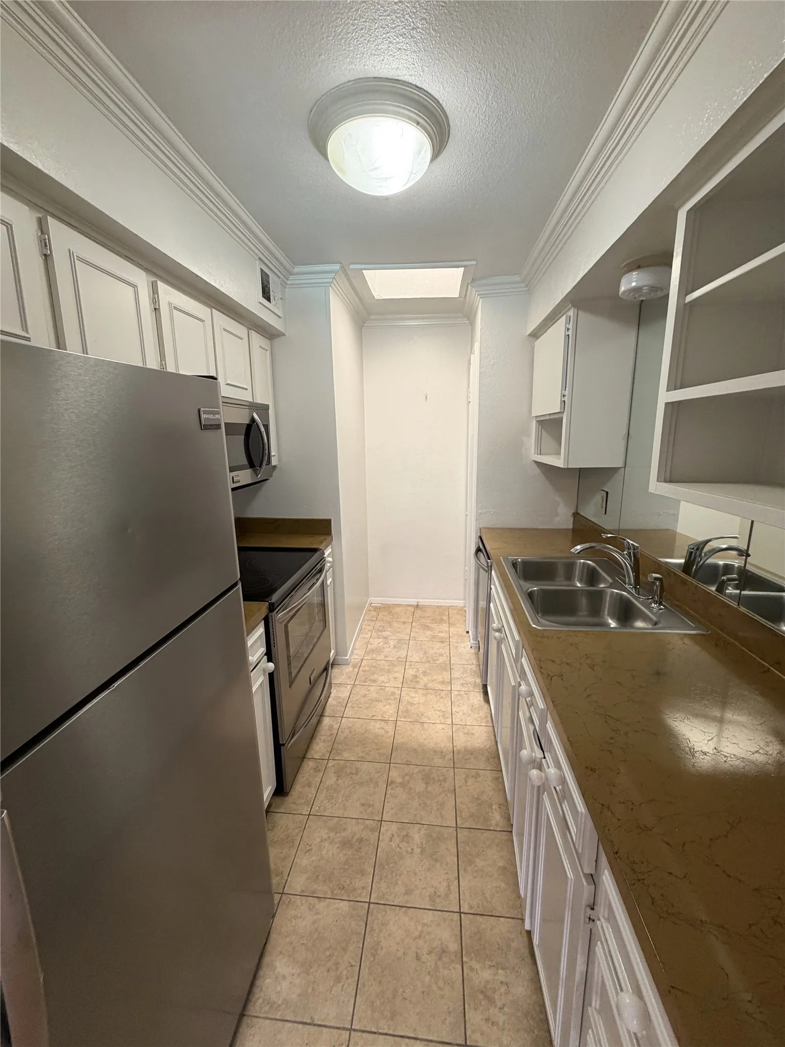 Galley kitchen featuring stainless steel appliances, tiled flooring, white cabinetry, and a double basin sink
