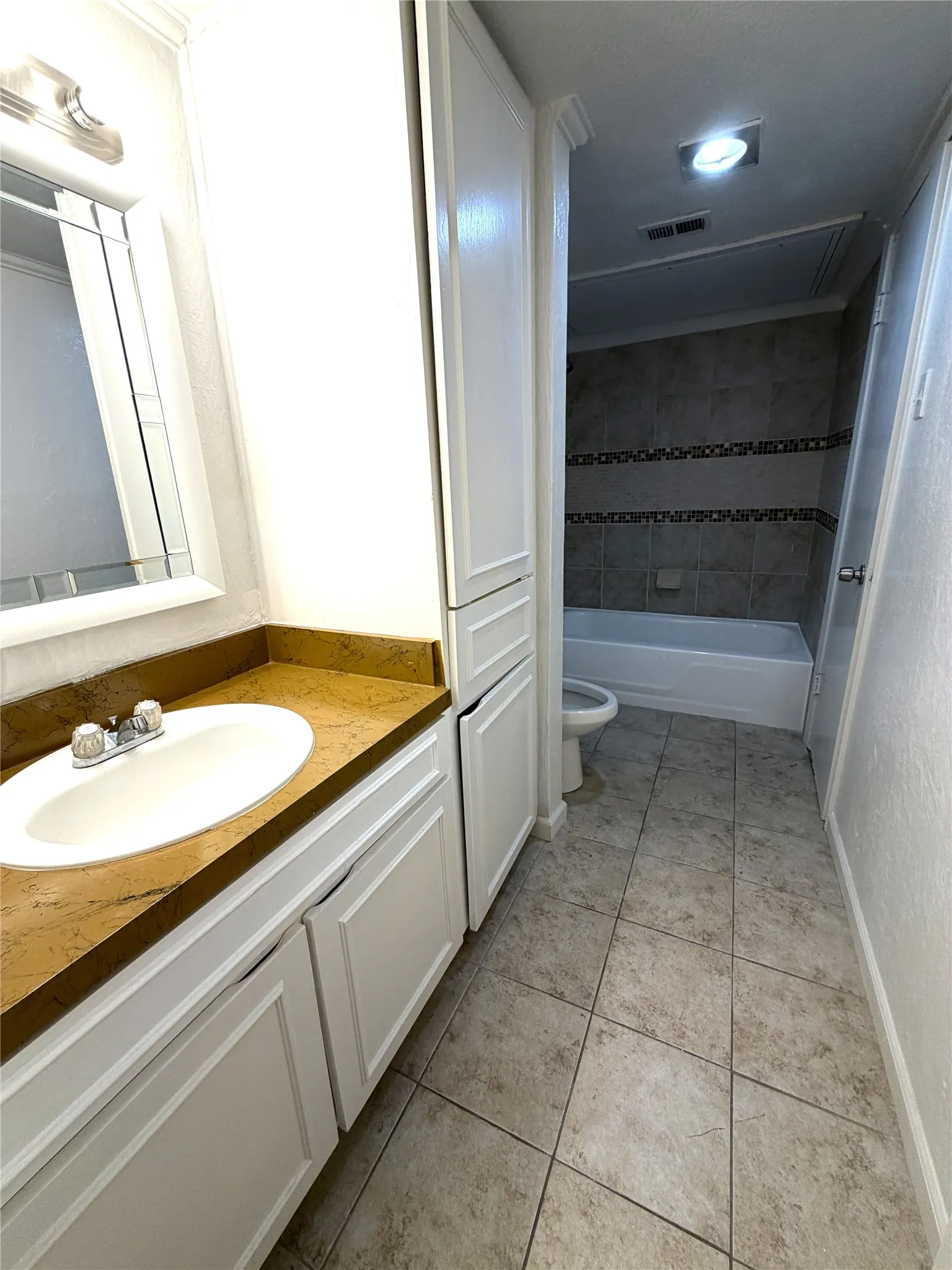 Bathroom featuring a vanity with a drop-in sink, solid surface countertop, white cabinetry, tiled flooring, and a tiled shower/tub combination