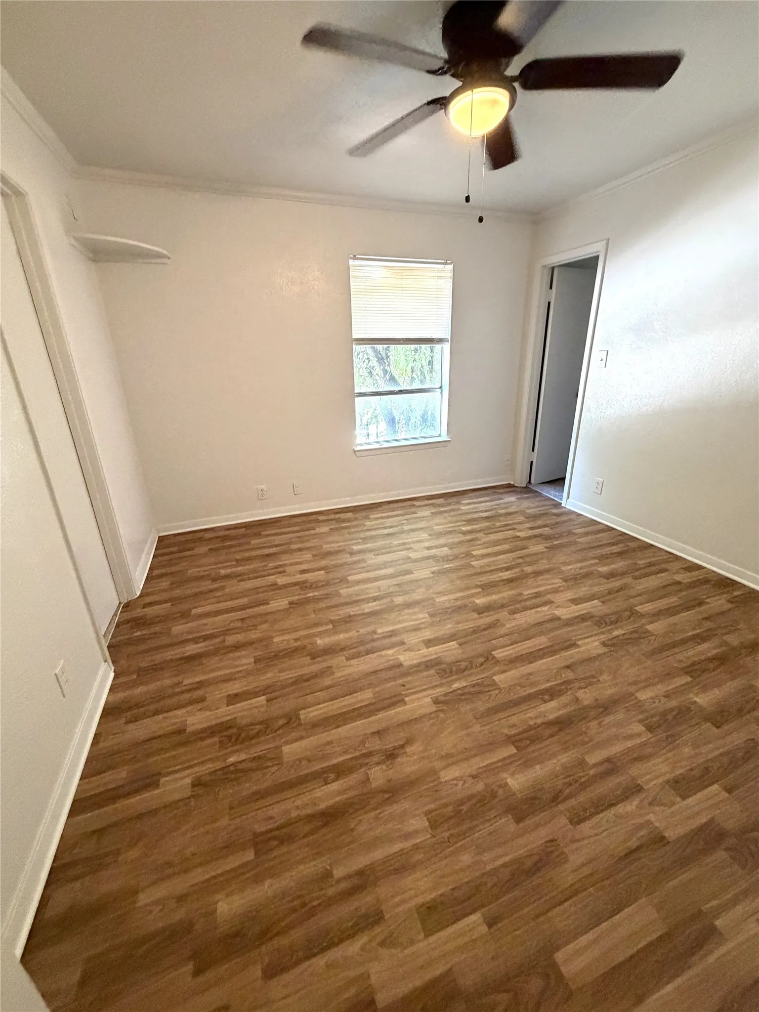 Wood-finish flooring, ceiling fan with integrated lighting, window with blinds, and crown molding
