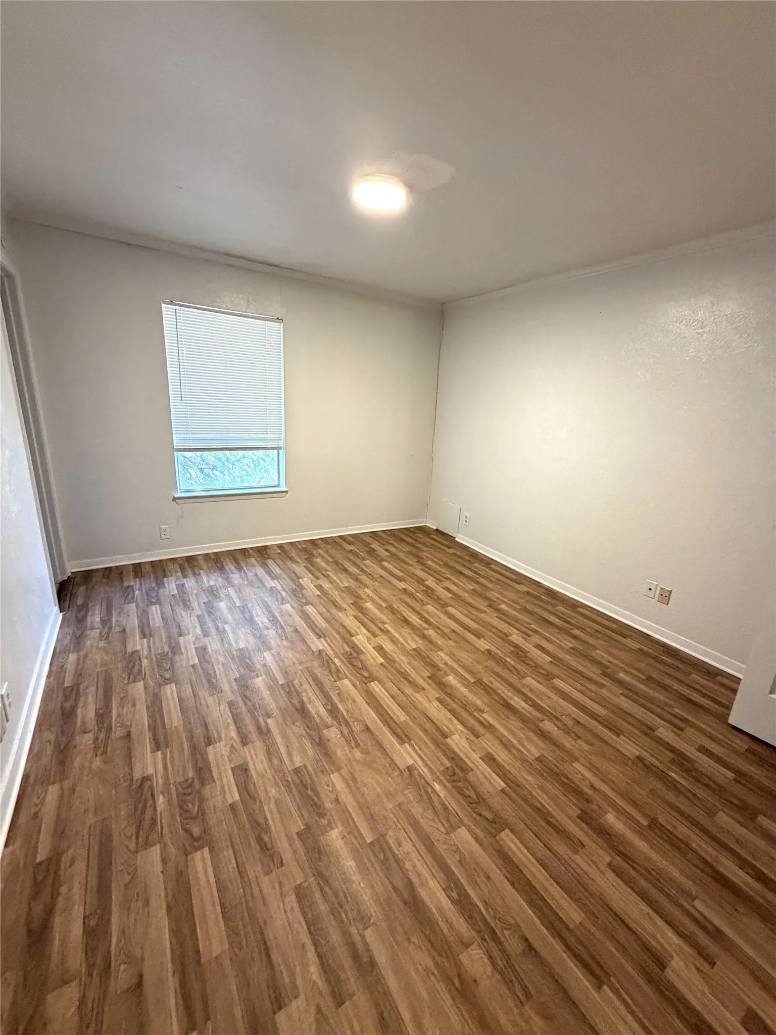 Wood-finish flooring throughout, white walls, and a recessed window with blinds