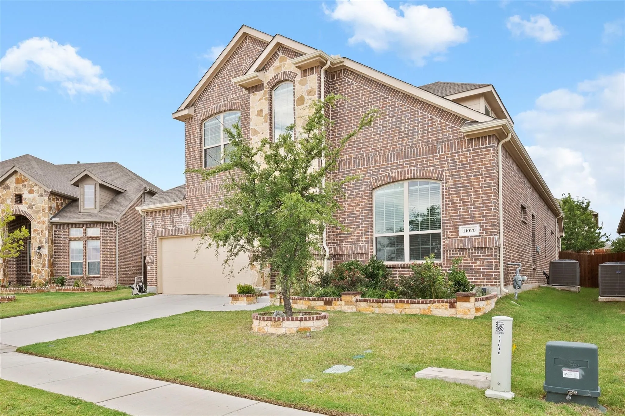 Brick and stone exterior featuring an attached garage, landscaped front yard, concrete driveway, and established shrubbery