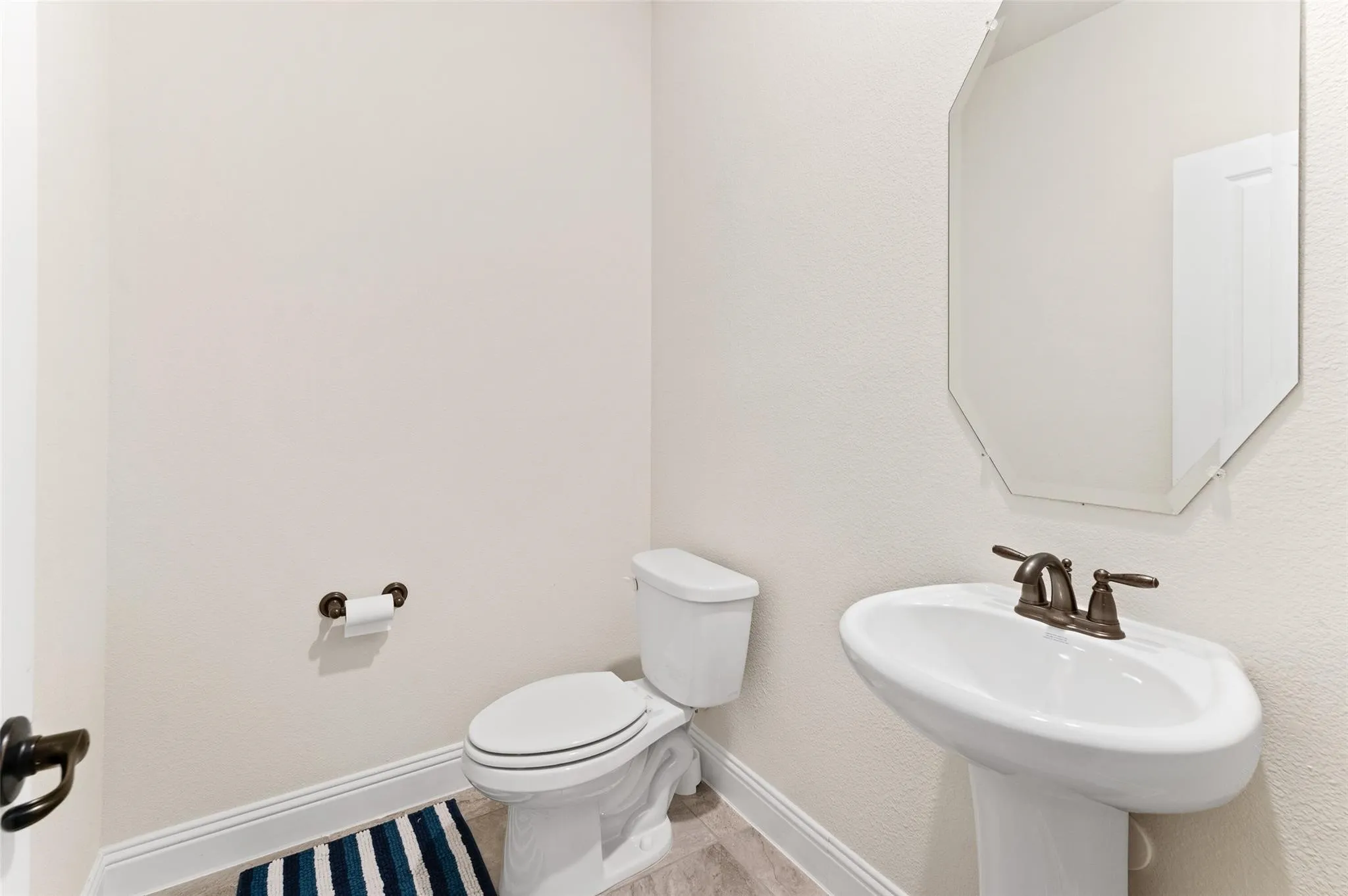 Pedestal sink with bronze-finish faucet, octagonal frameless mirror, and neutral wall paint