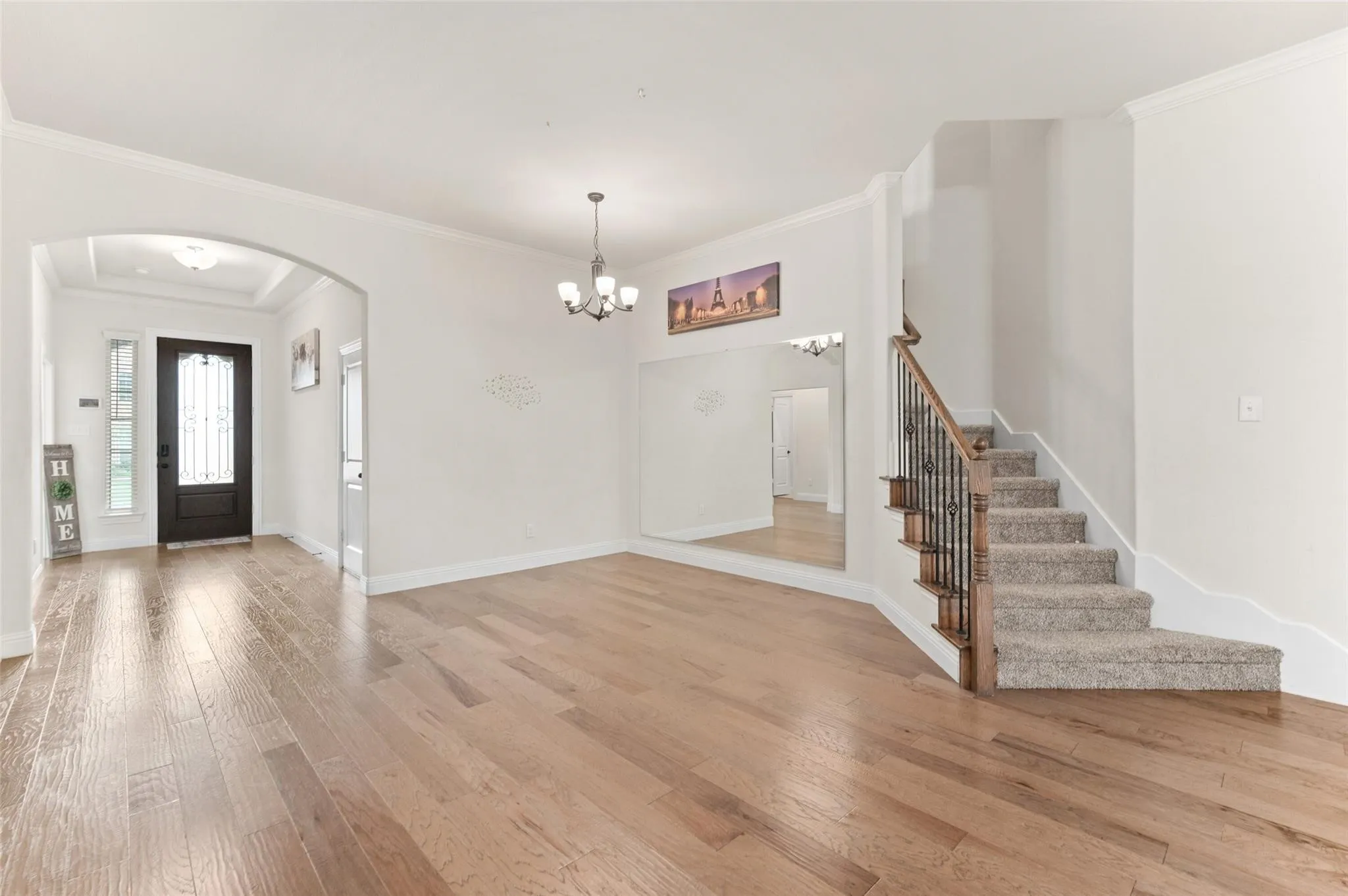 Arched entryway with a coffered ceiling, wood-finish flooring, staircase with wrought iron balusters, and a chandelier