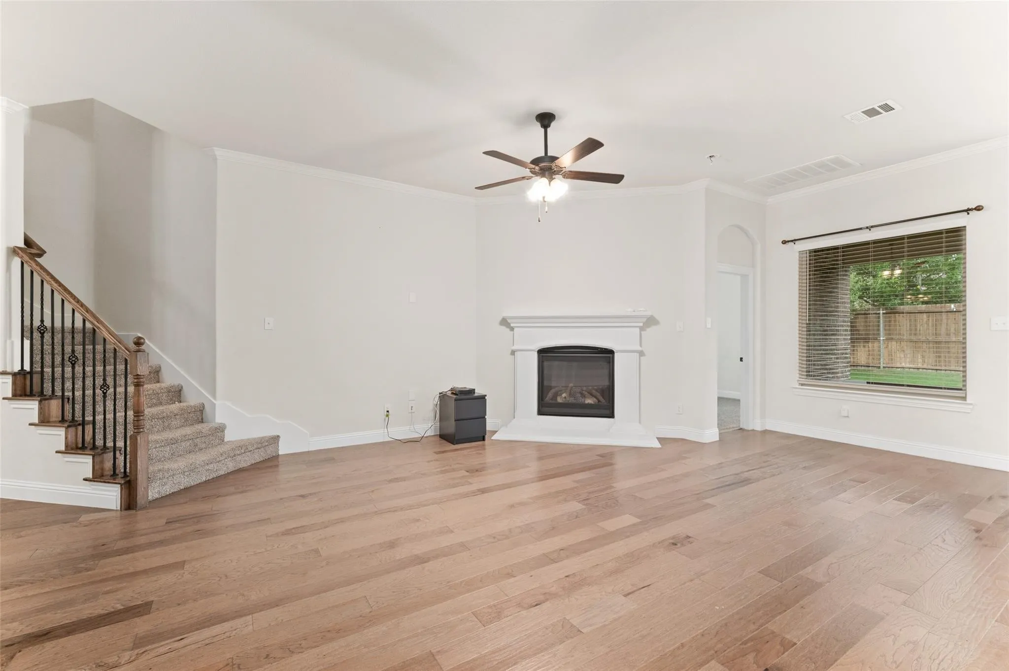 Wood-finish flooring throughout, featuring a fireplace with a white mantel, a ceiling fan, and a chandelier