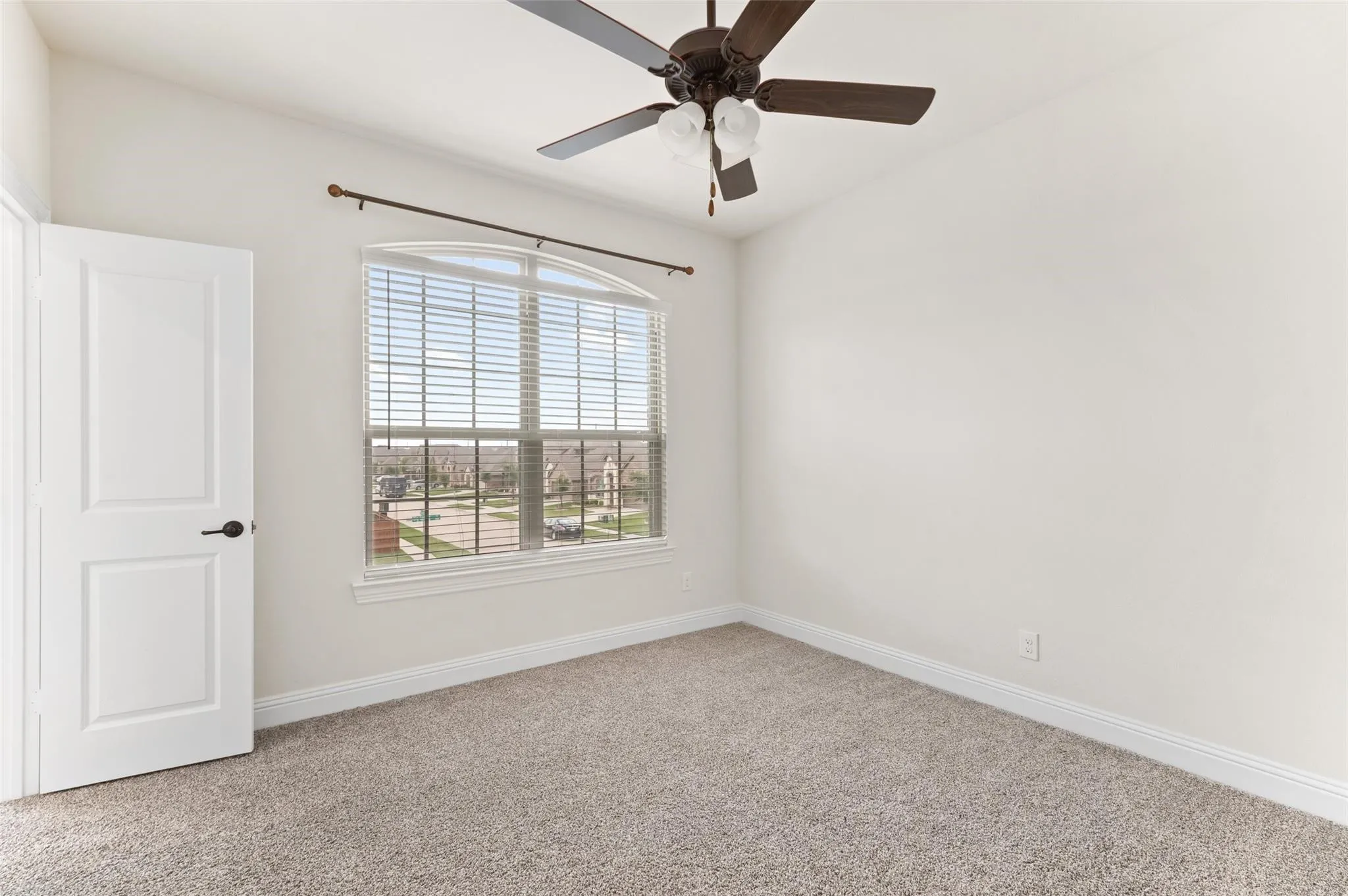 Arched window with blinds, overhead ceiling fan with light fixture, neutral carpeting, and a paneled door with dark hardware