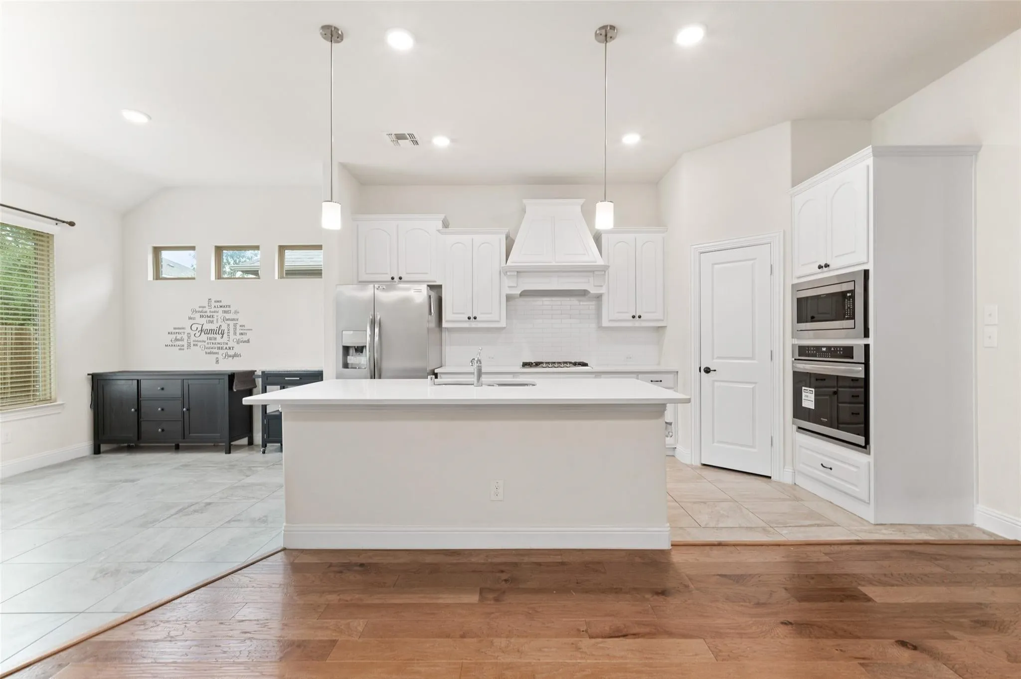 Open-concept kitchen featuring an island with a dual-basin sink, white cabinetry with crown molding, stainless steel appliances, and wood-finish flooring