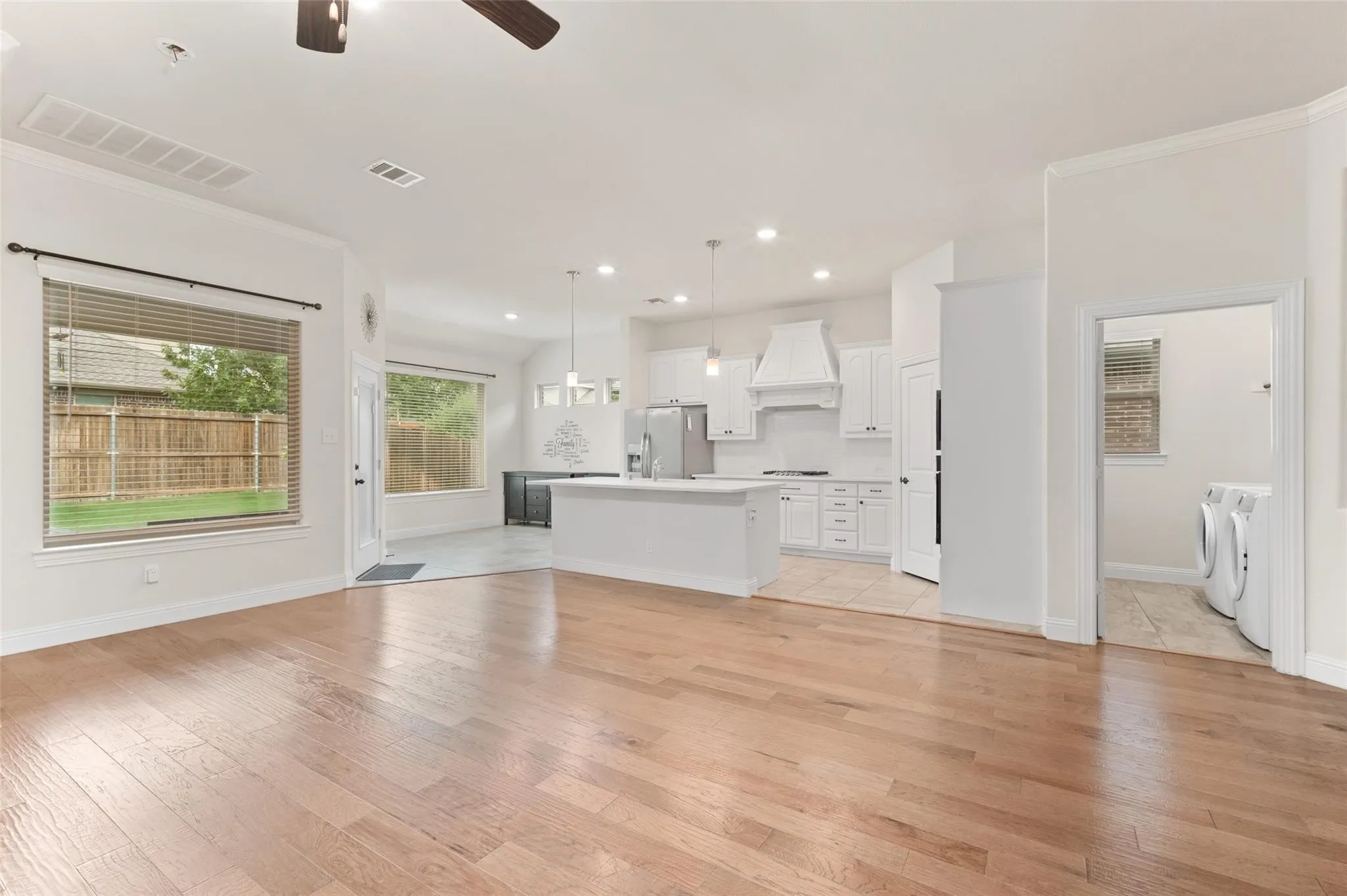 Hardwood flooring, crisp white walls, recessed lighting, white kitchen cabinetry, and a kitchen island with seating