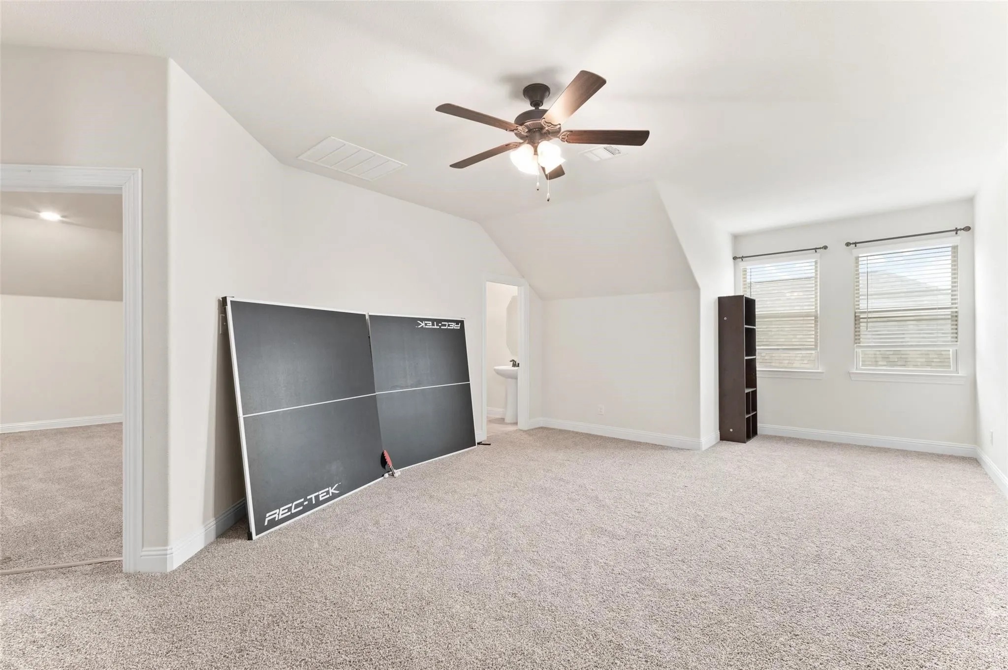 Expansive carpeted room featuring a ceiling fan, dual windows with blinds, and white painted walls