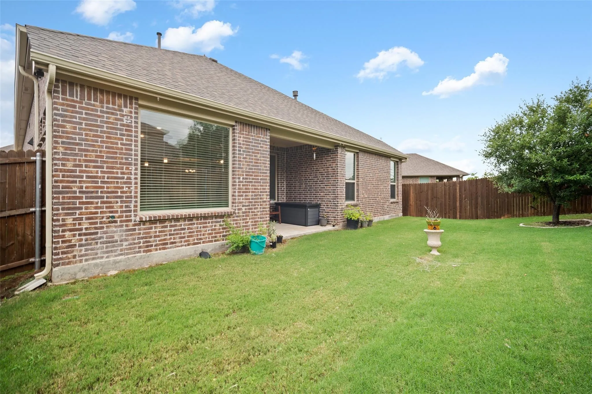 Expansive grassy yard with a covered patio, brick exterior, and wood fencing